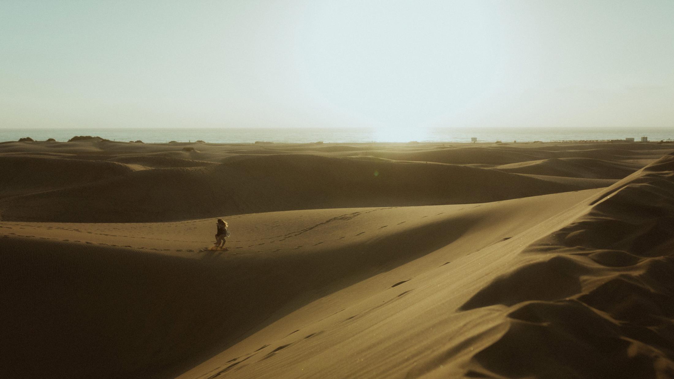 A lone figure running across a sunlit dune with the ocean beyond.
