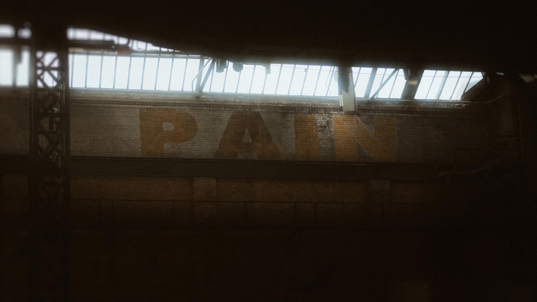 The word PAIN painted high across the brick wall inside Mahalla in Berlin.
