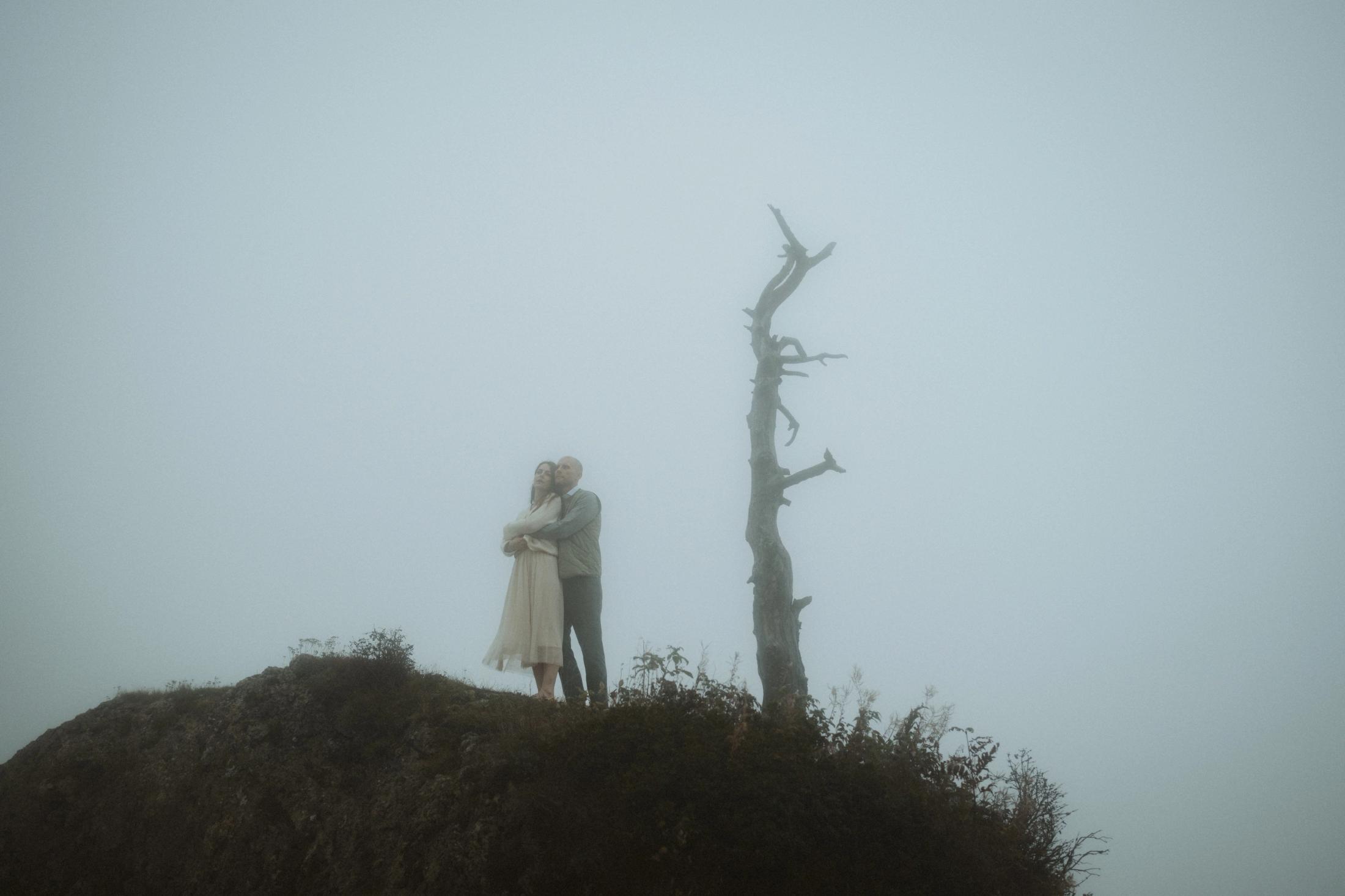 Jana and Steffen beside a bare tree on a rocky rise in the fog.