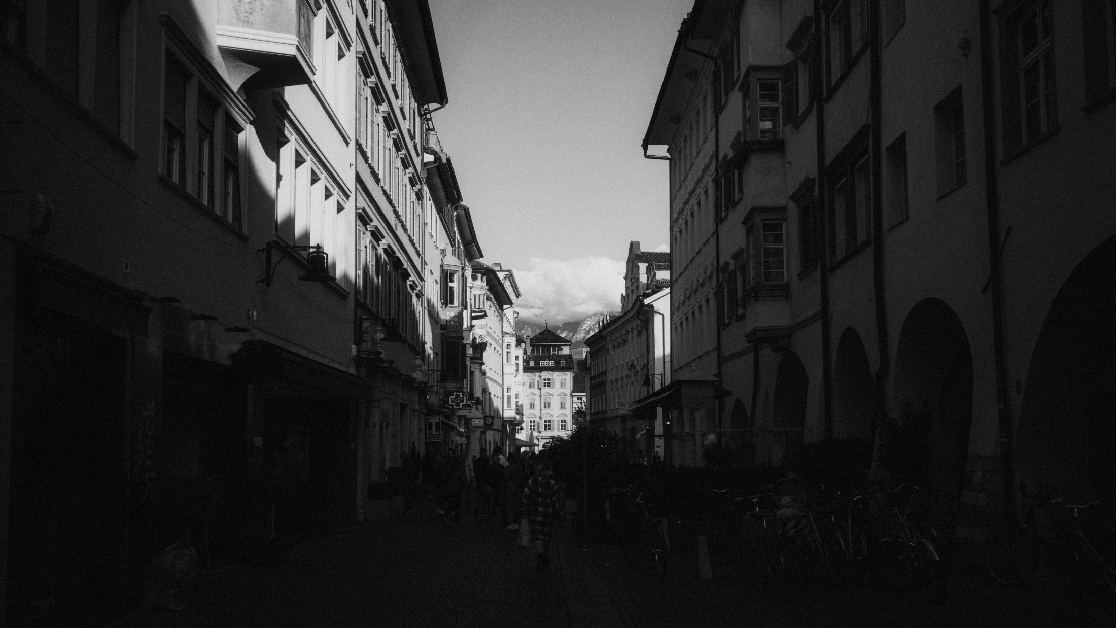 A dark street in Bolzano with a small figure walking beneath the surrounding buildings.