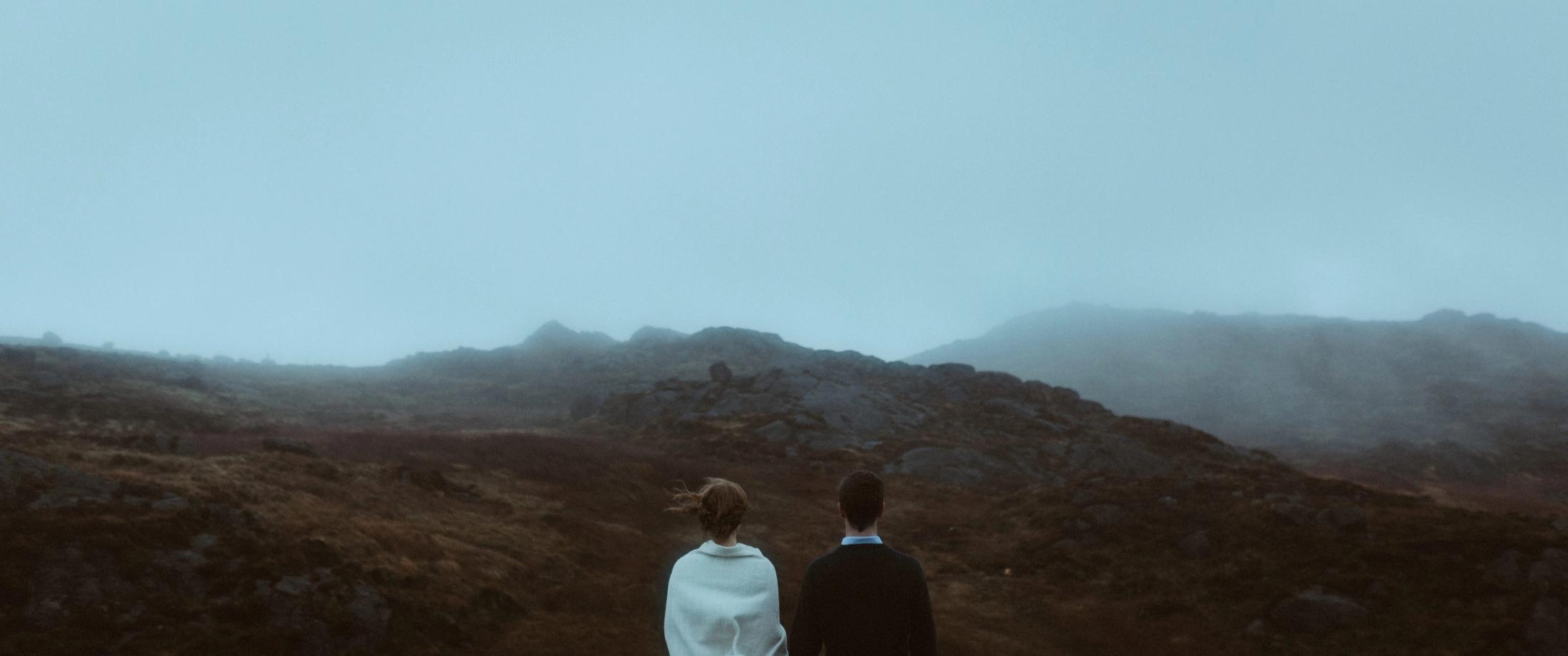 Jule und Rory stehen klein auf Felsen über der Küste, ihr weißes Kleid bewegt sich im Wind.