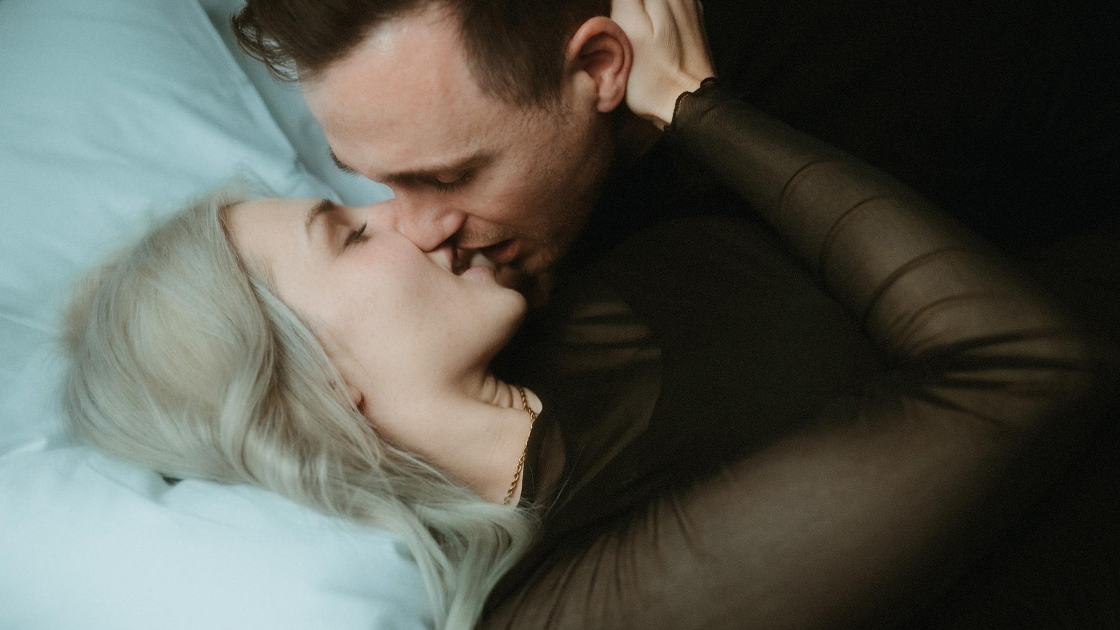 Steffen leans down to kiss Lorelai on the hotel bed.