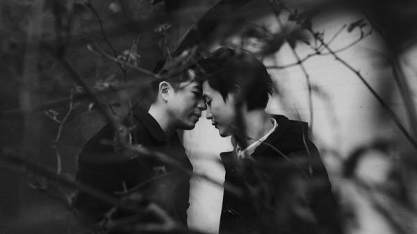 Kevin and Terence touch foreheads in a black-and-white portrait framed by bare branches.