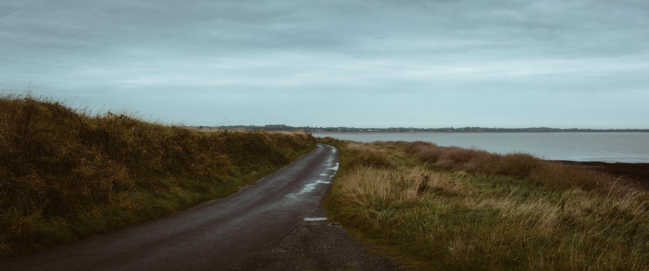Leere Küstenstraße zwischen braunen Hügeln unter bewölktem Himmel in County Louth, Irland.