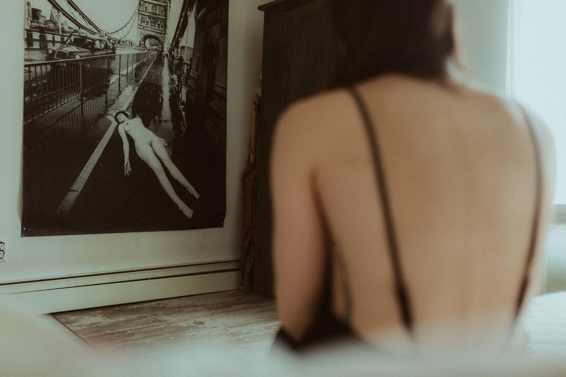 Maya seen from behind beside a large black-and-white nude artwork.