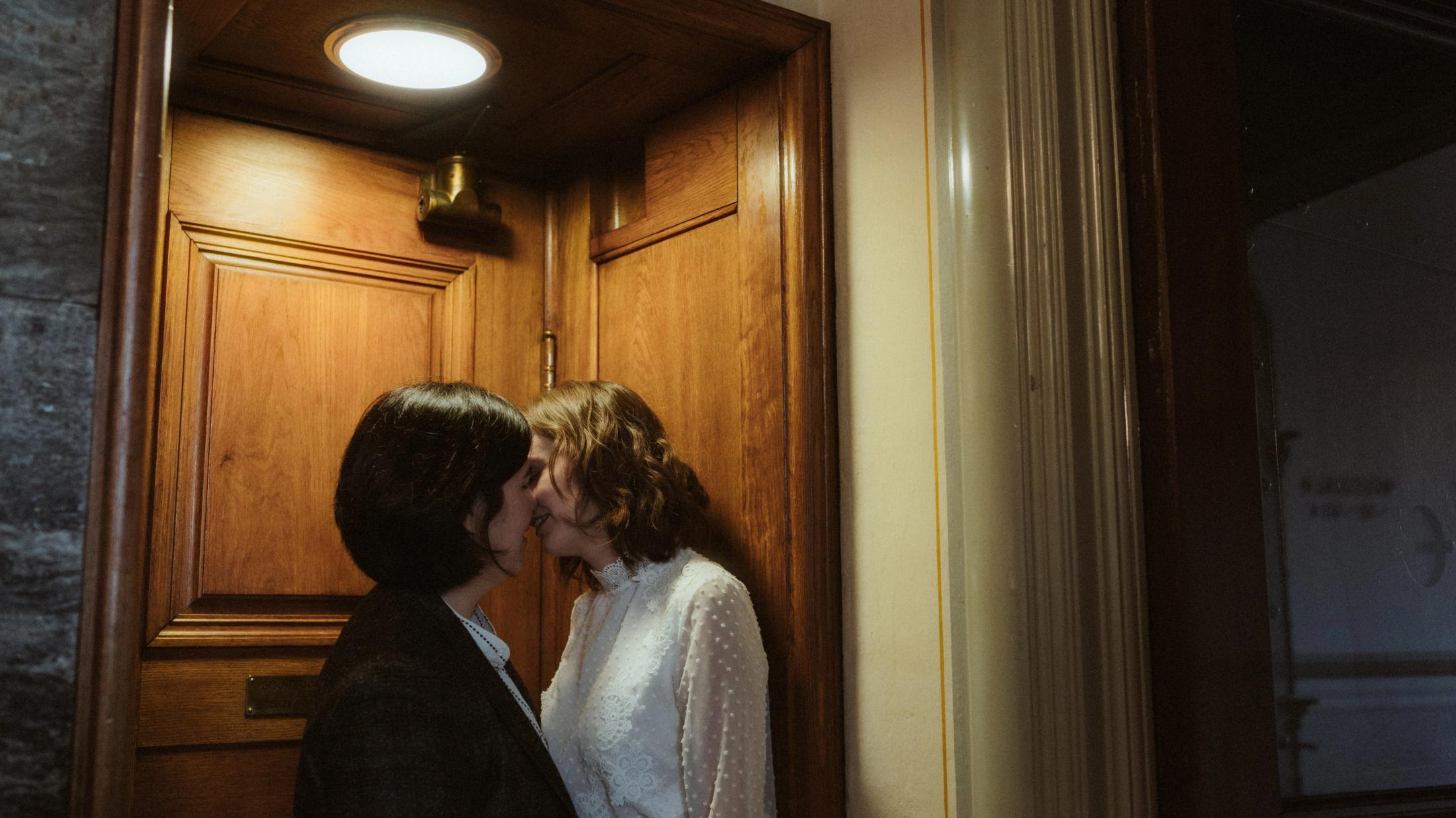 Ari and Pia kissing inside a dark wooden doorway