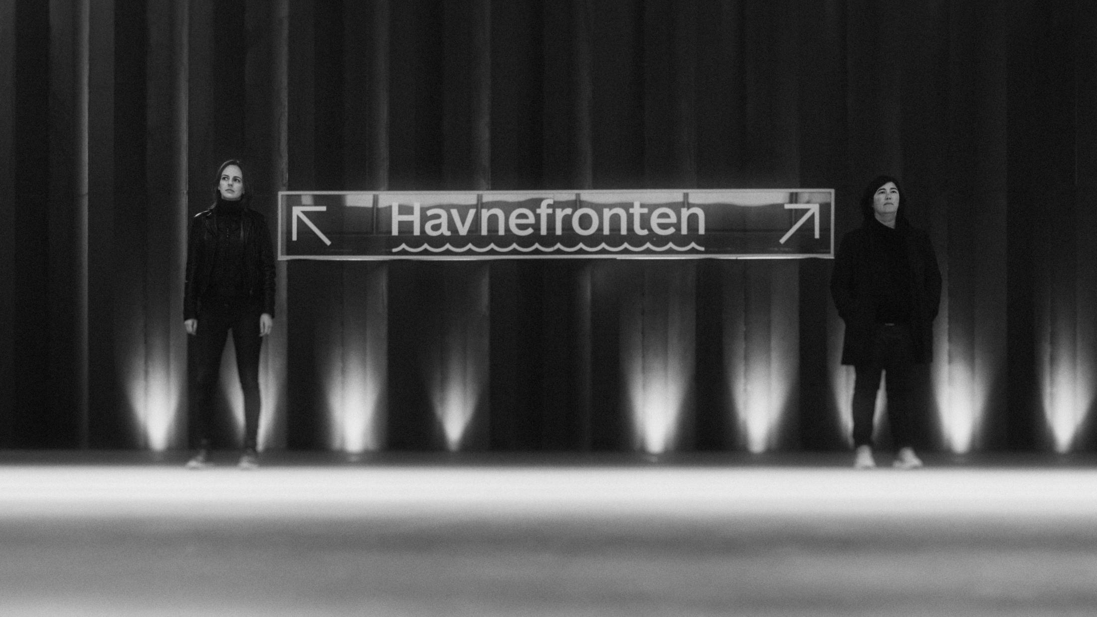Ari and Pia standing apart beside a Havnefronten sign at night