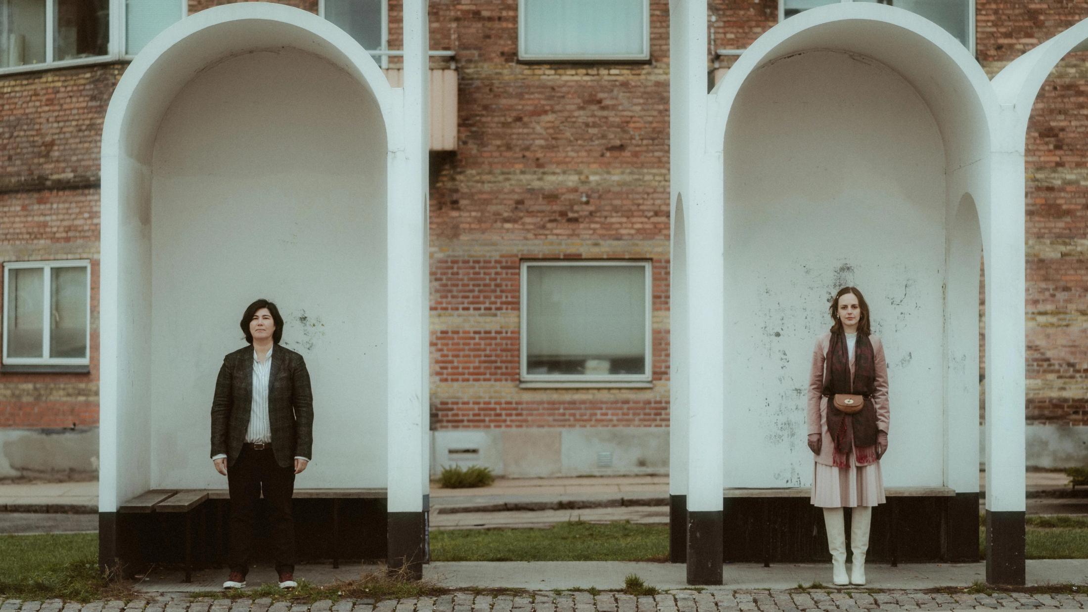 Ari and Pia standing separately in white arched recesses