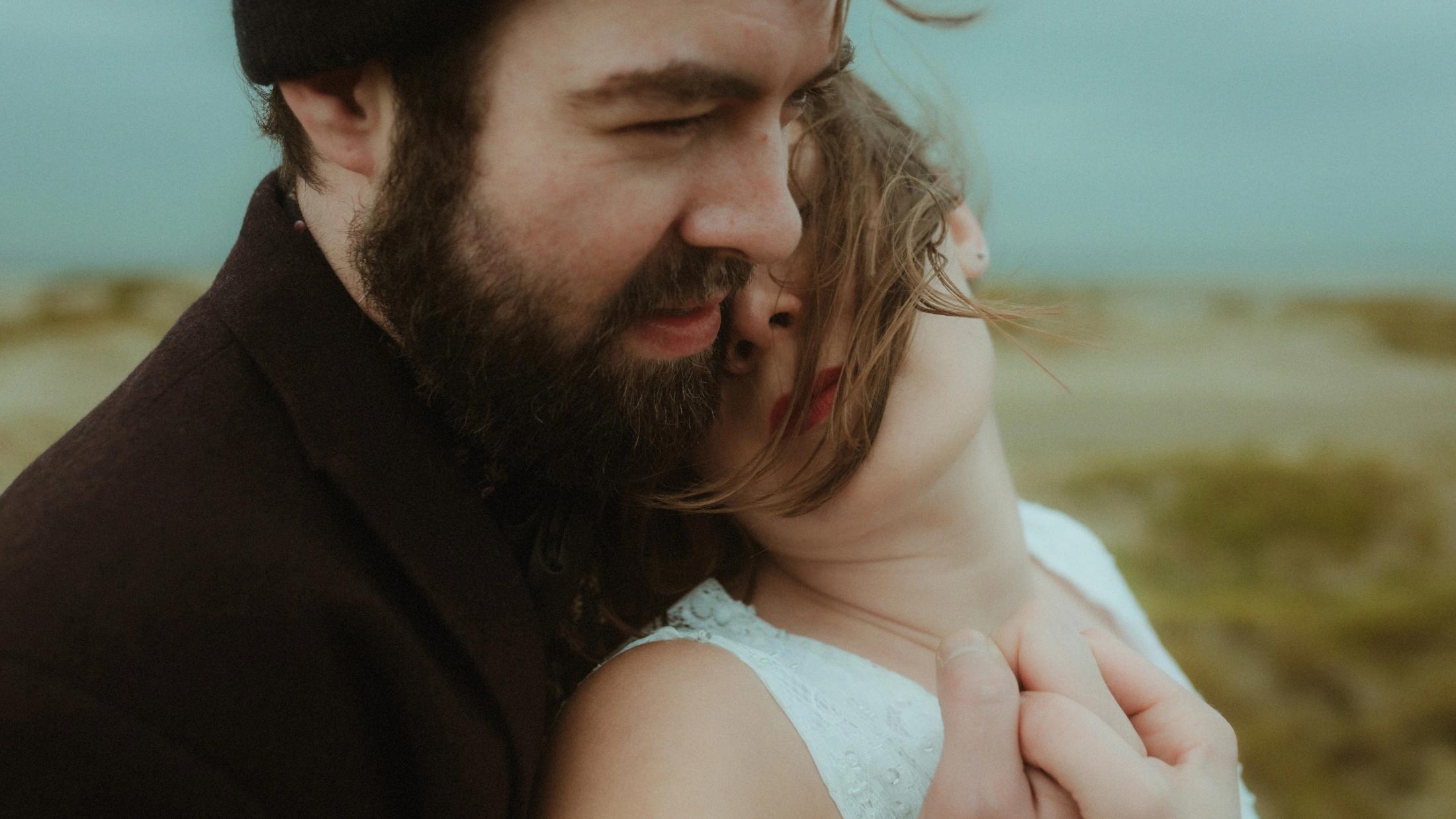 Daniel holds Anni close near the dunes as the wind moves her hair.