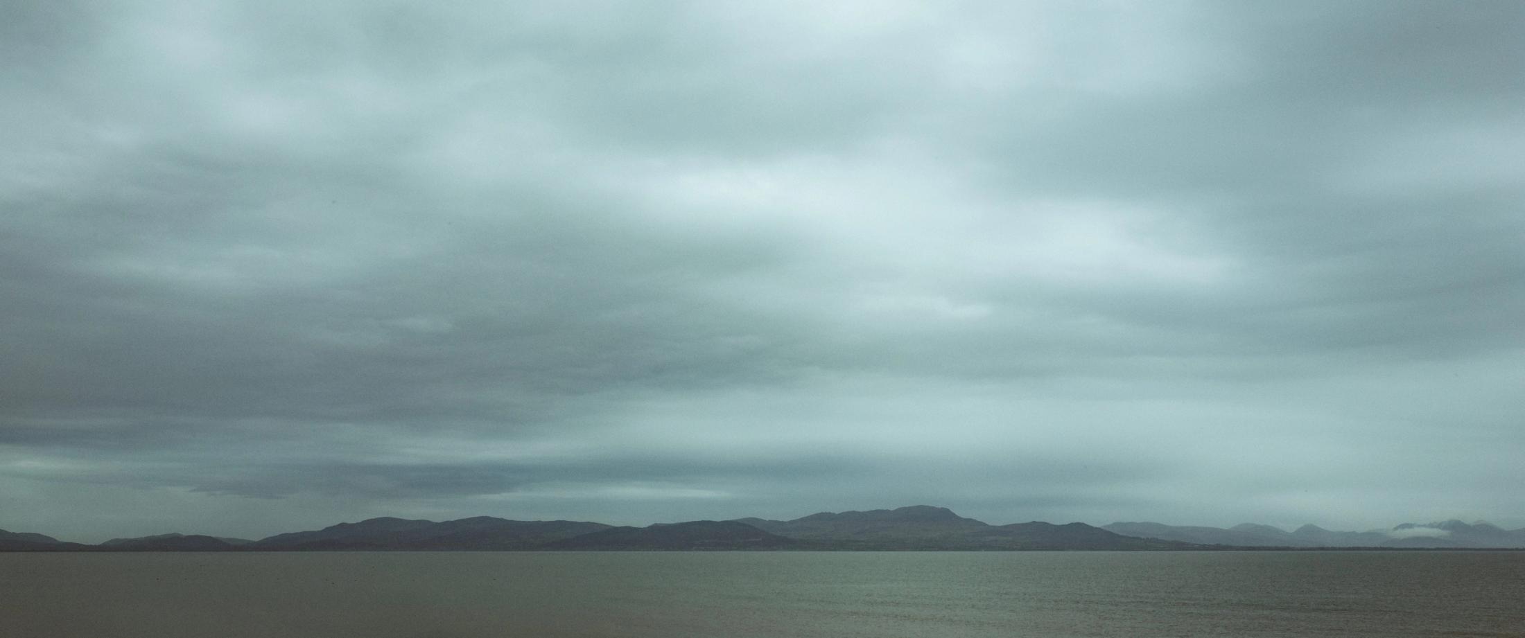Weiter Blick über Carlingford Lough zu fernen Hügeln unter schwerem grauem Himmel.