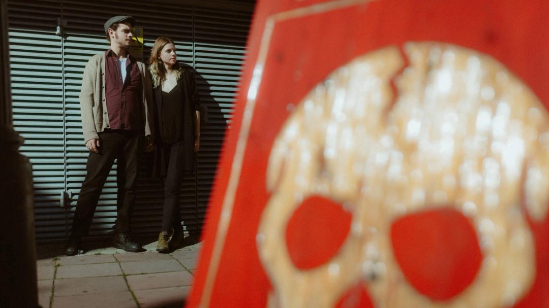 Aiste and John framed by a bold red street detail in Brighton