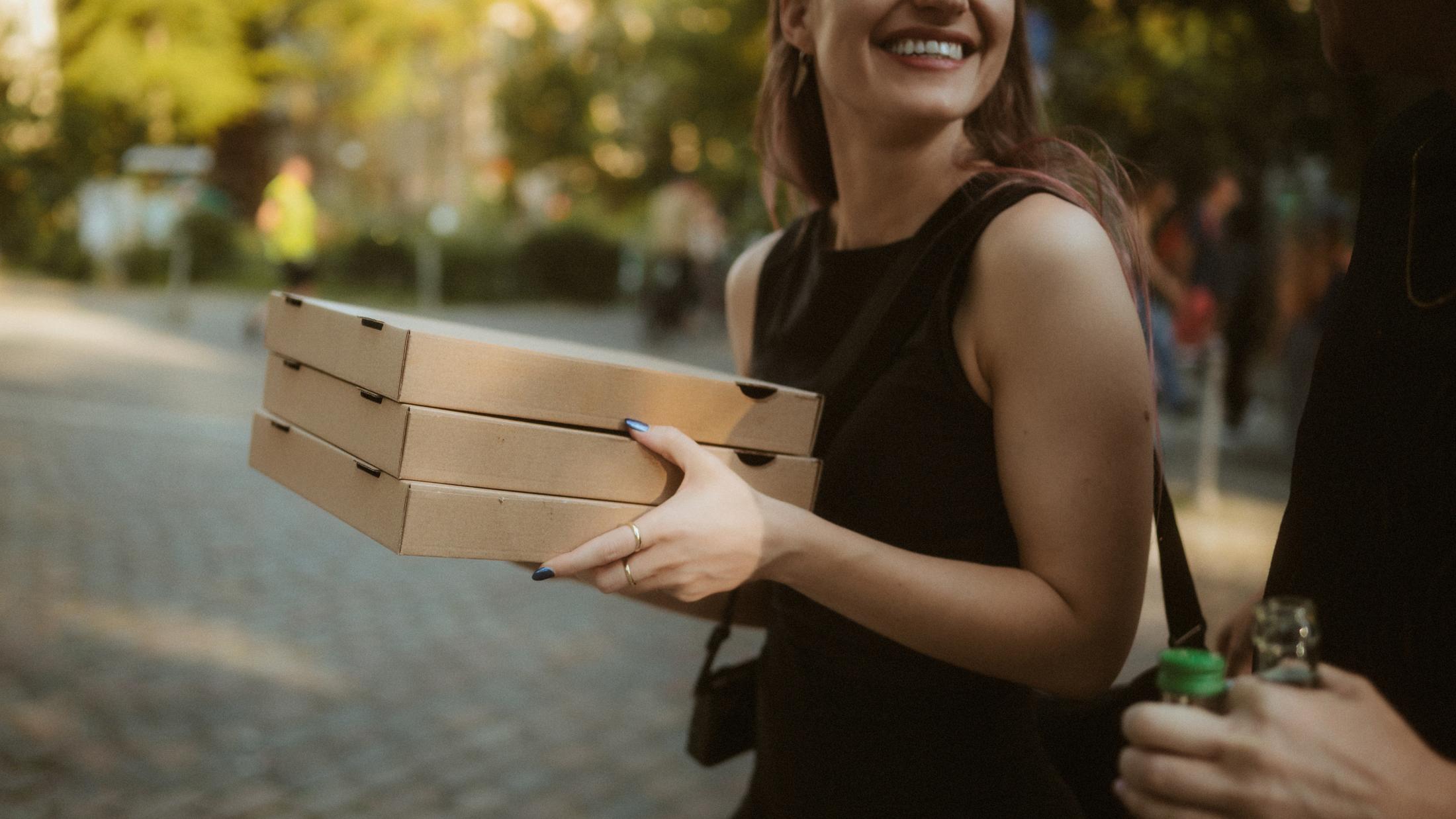 Michèle smiling while carrying stacked pizza boxes near the Landwehrkanal.