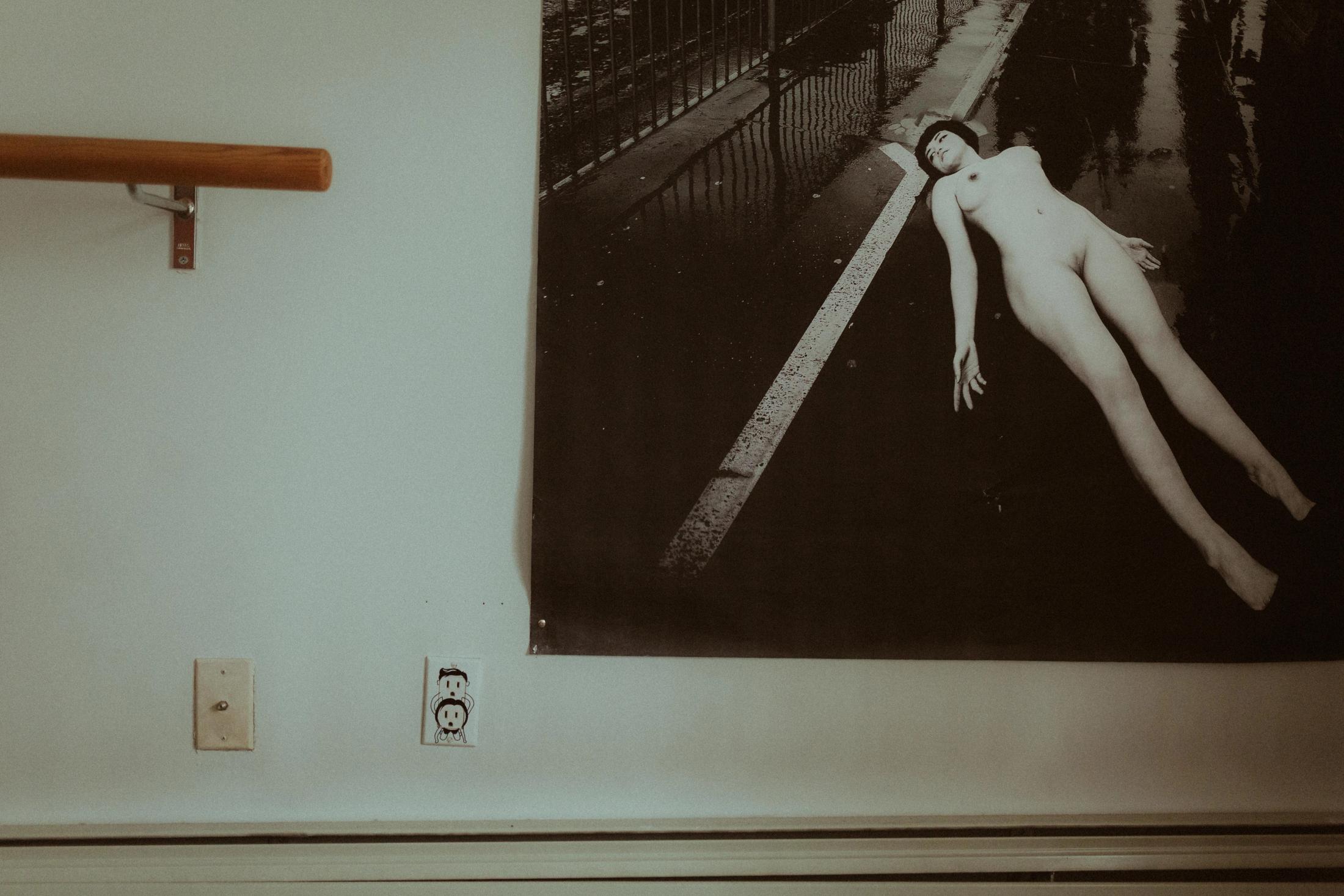 A large black-and-white nude artwork hanging in Maya’s apartment.
