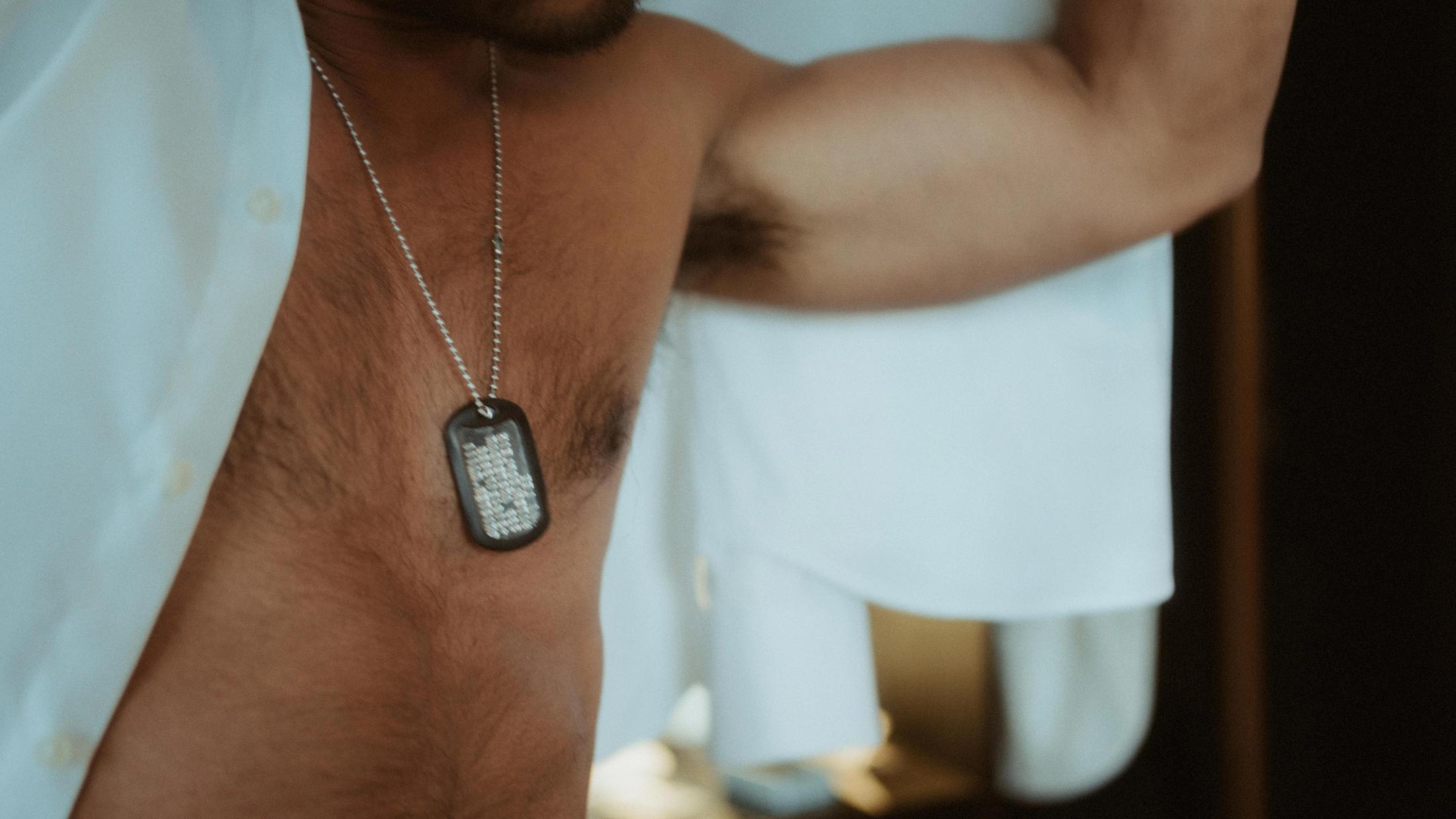 Close view of Kris's metal dog tag resting against his bare chest.