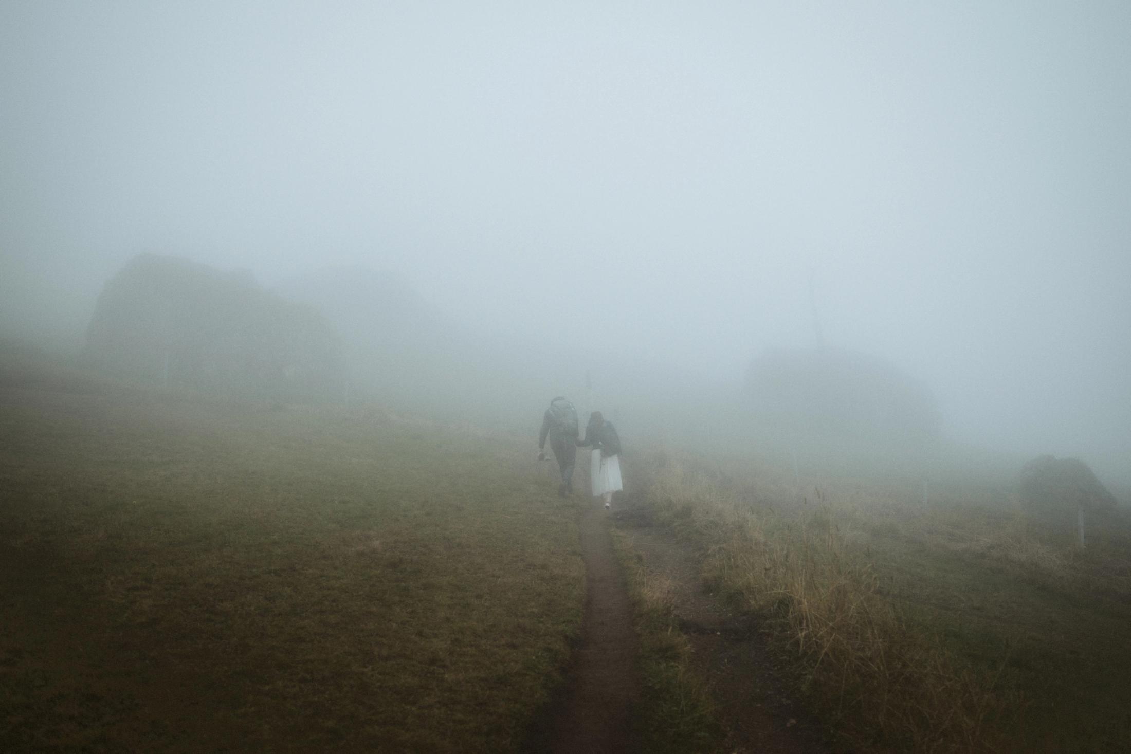 Jana and Steffen becoming small shapes as they walk into thick fog.
