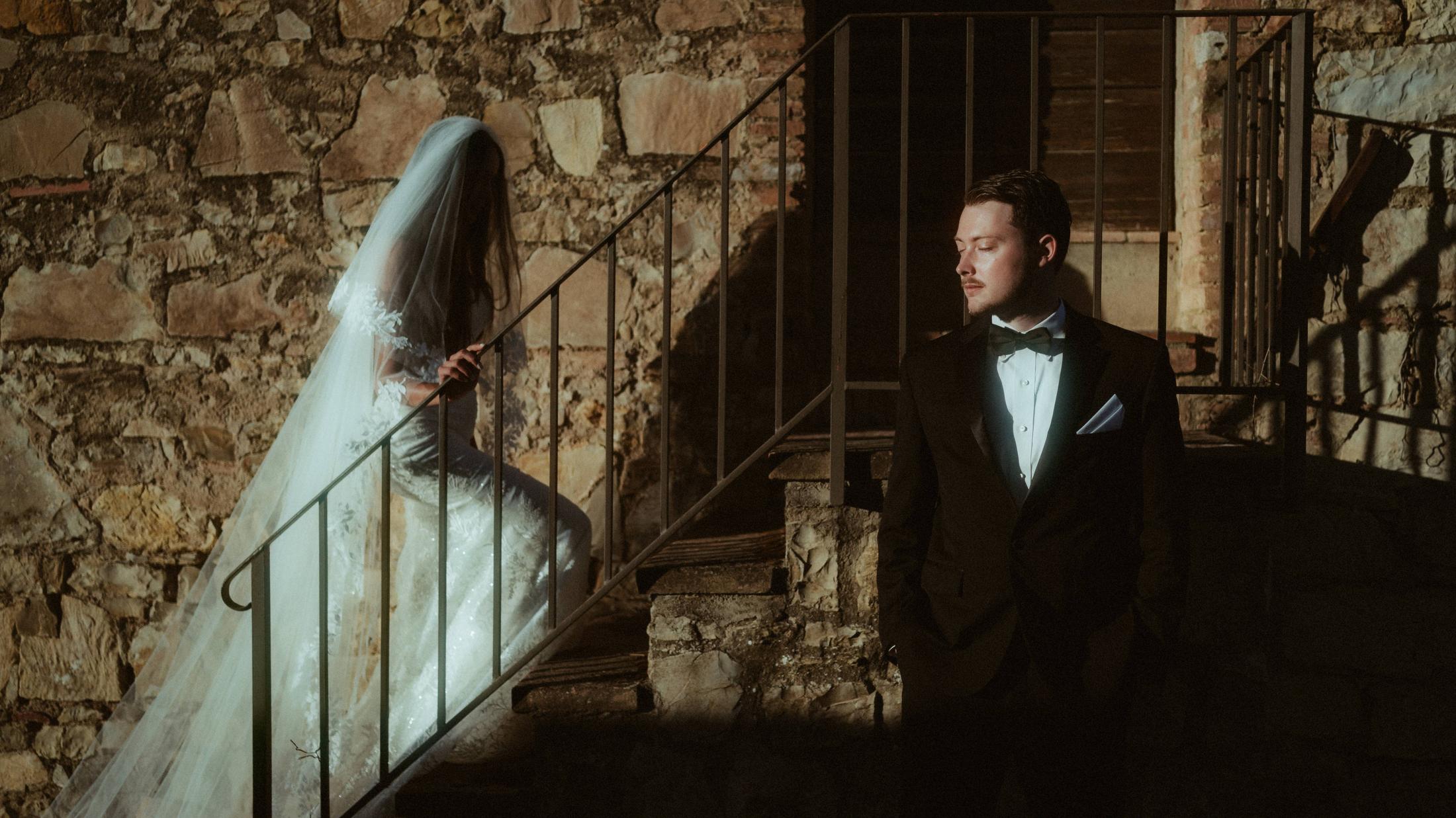 The couple stands apart on a narrow stone staircase in Tuscany.