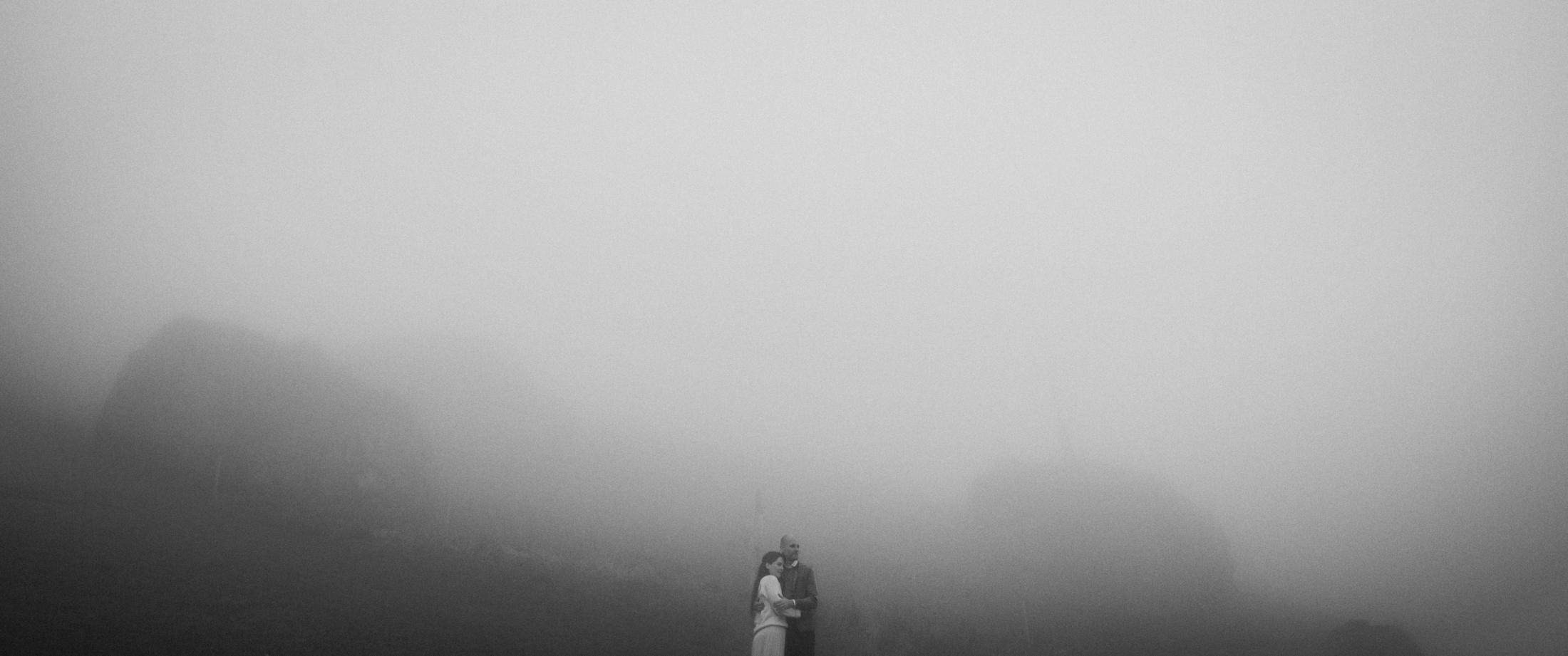 Jana and Steffen standing beneath a broad wall of fog in the mountains.