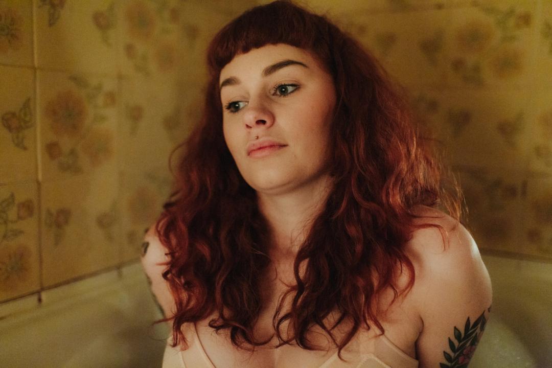 Laura sitting upright in soft interior light