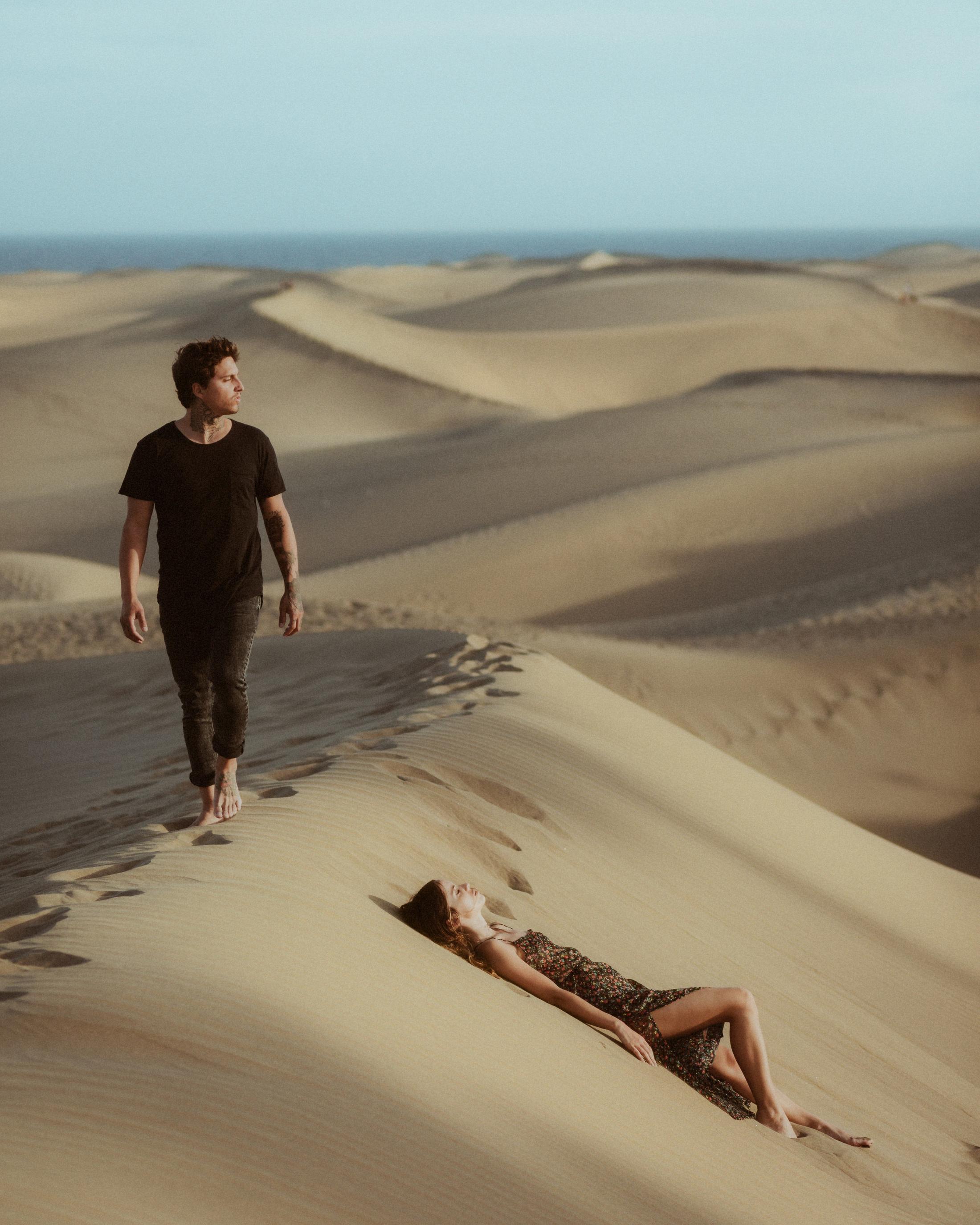 Angela und Ivan liegen im Sand und sehen sich an.