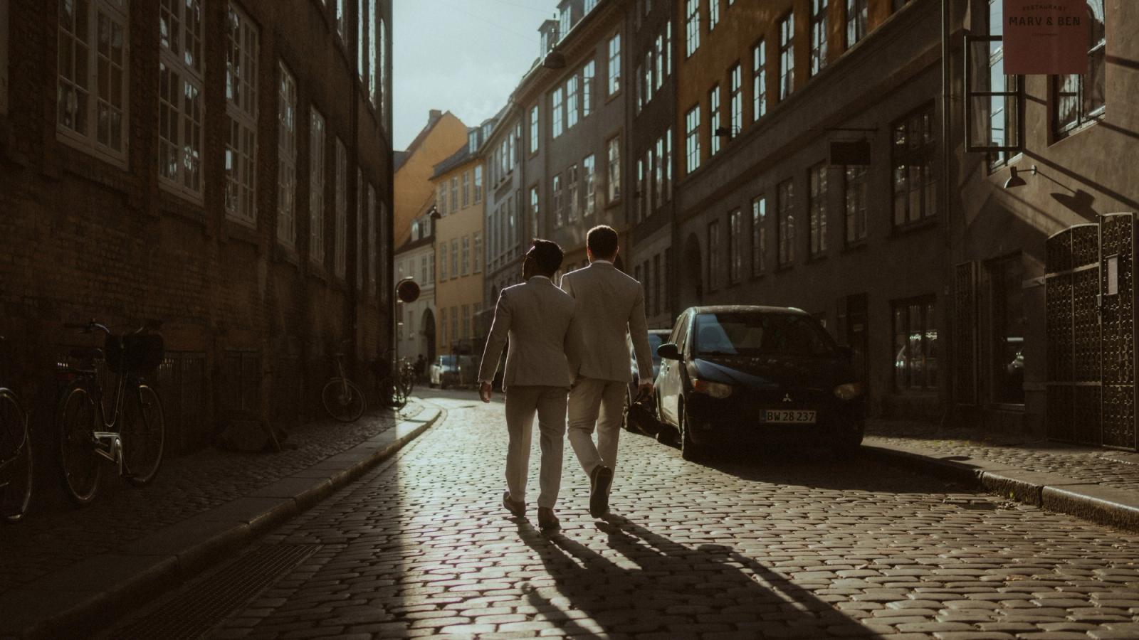 The couple walks away along a cobbled Copenhagen street in low evening light.