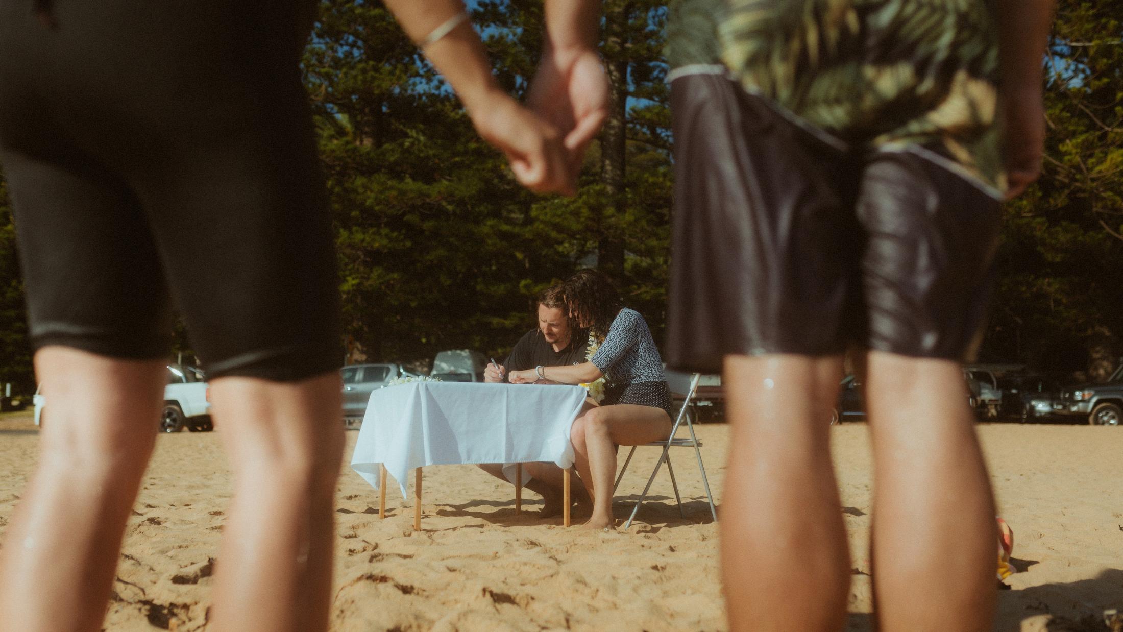 Petra and Roman signing at a small beach table between their standing witnesses