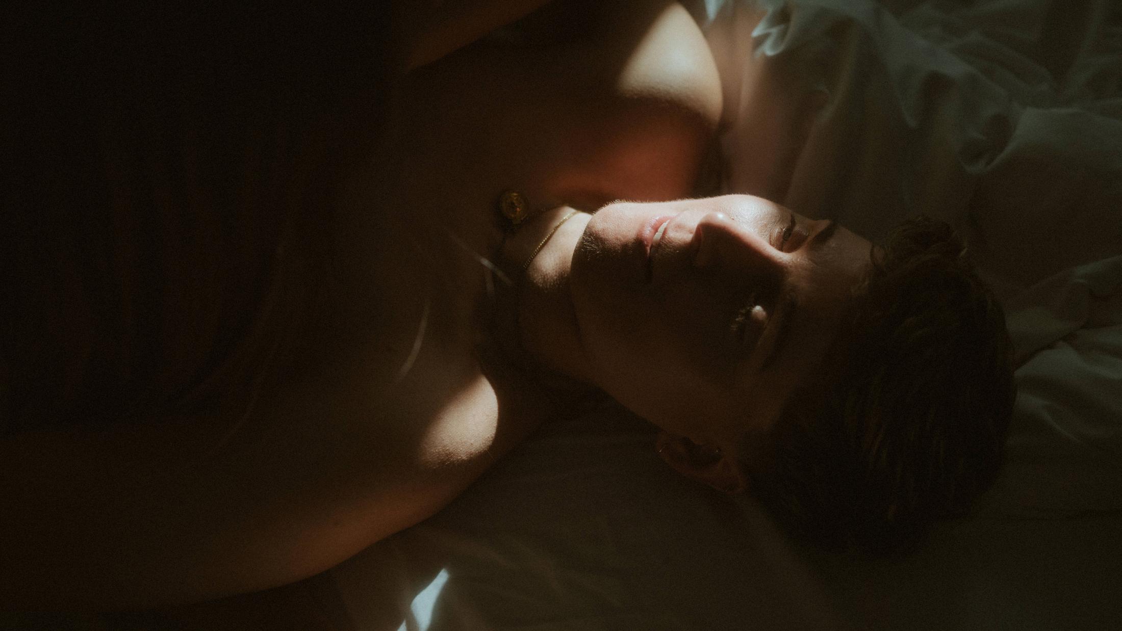 Noah lying alone with their face illuminated against a dark bed.