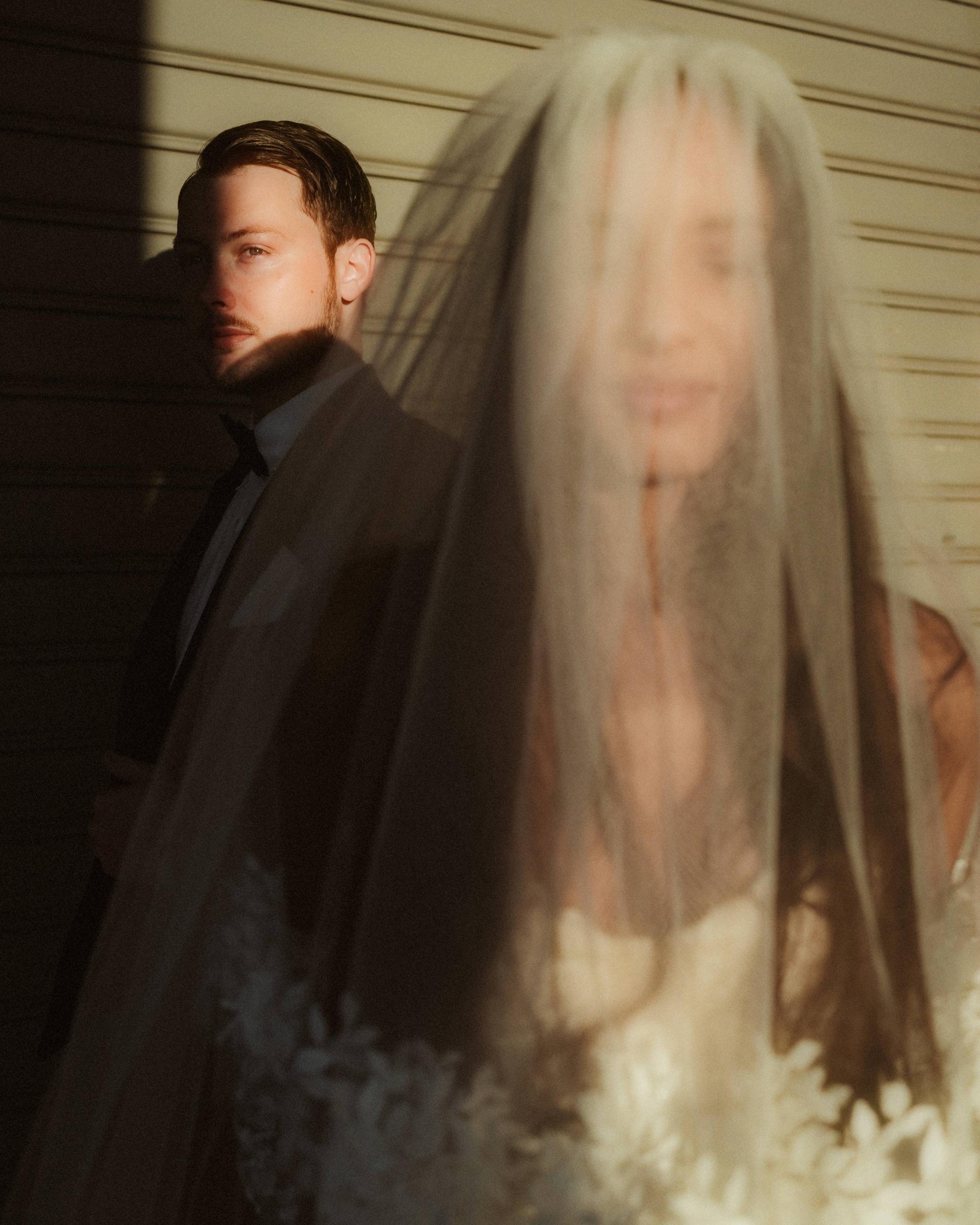 The bride's face appears softly through her moving veil in the morning sun.