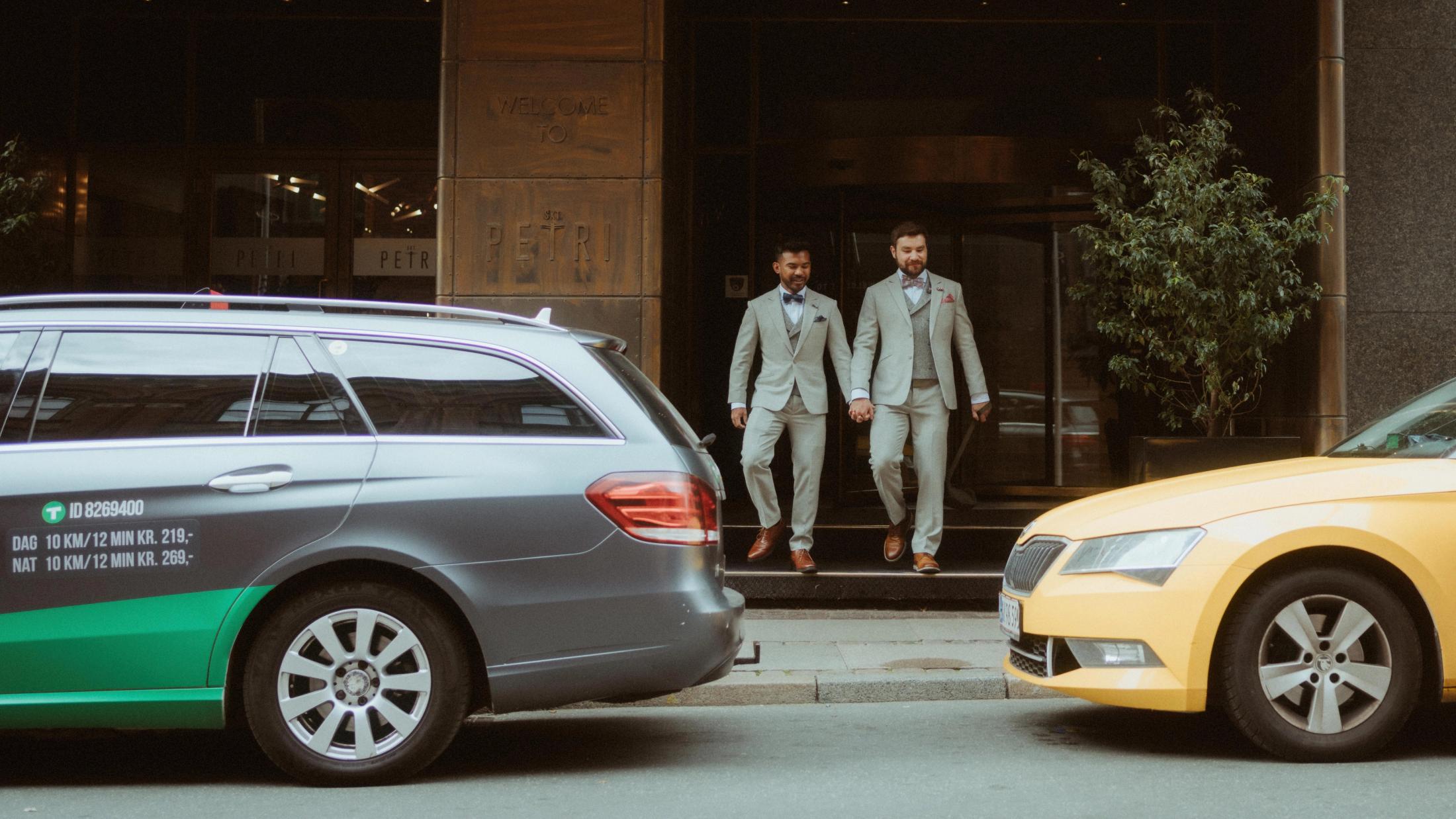 Kris and Ilya stand outside City Hall between two passing cars.