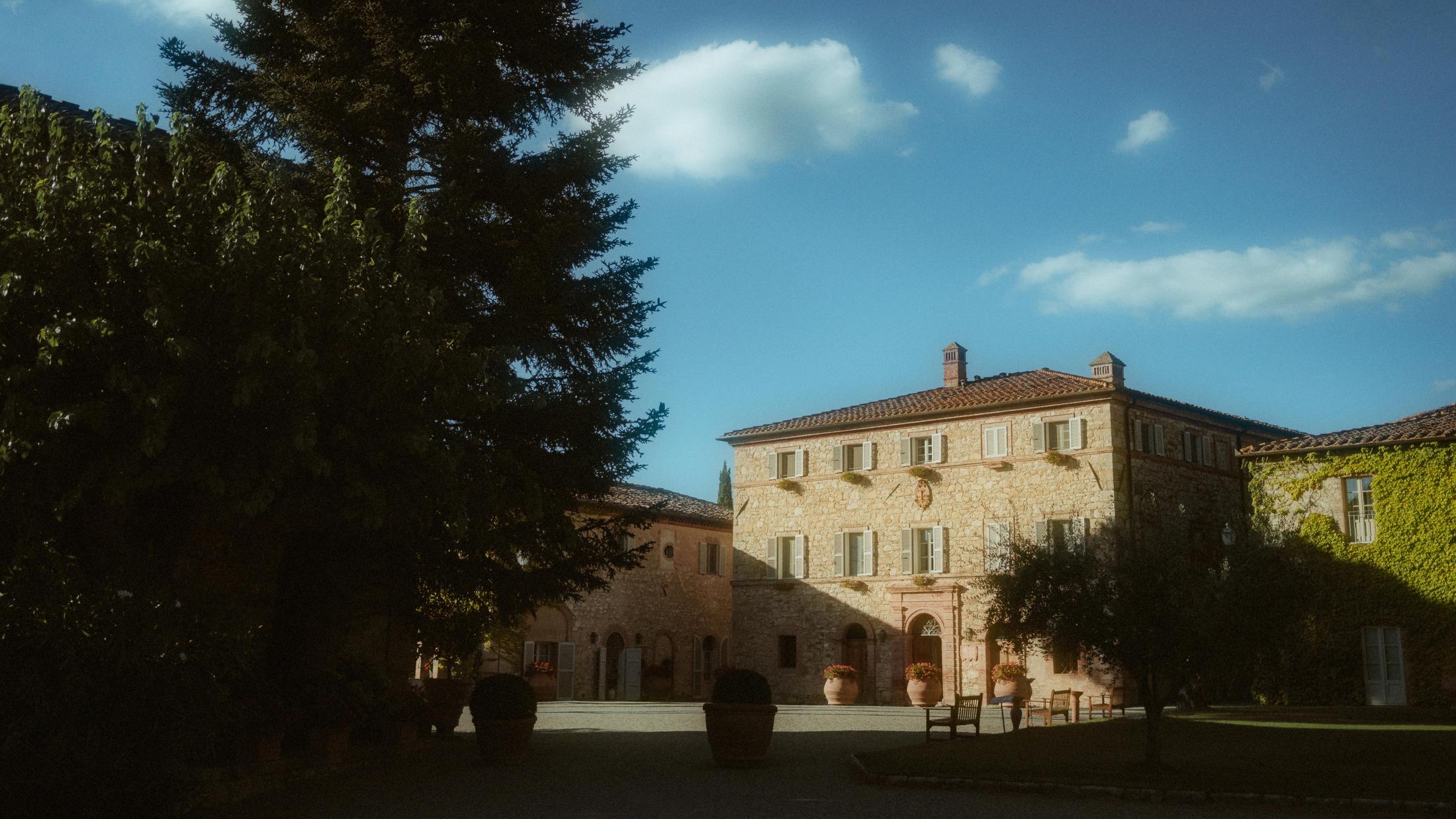 A stone building and tall tree at Borgo San Felice in the evening light.