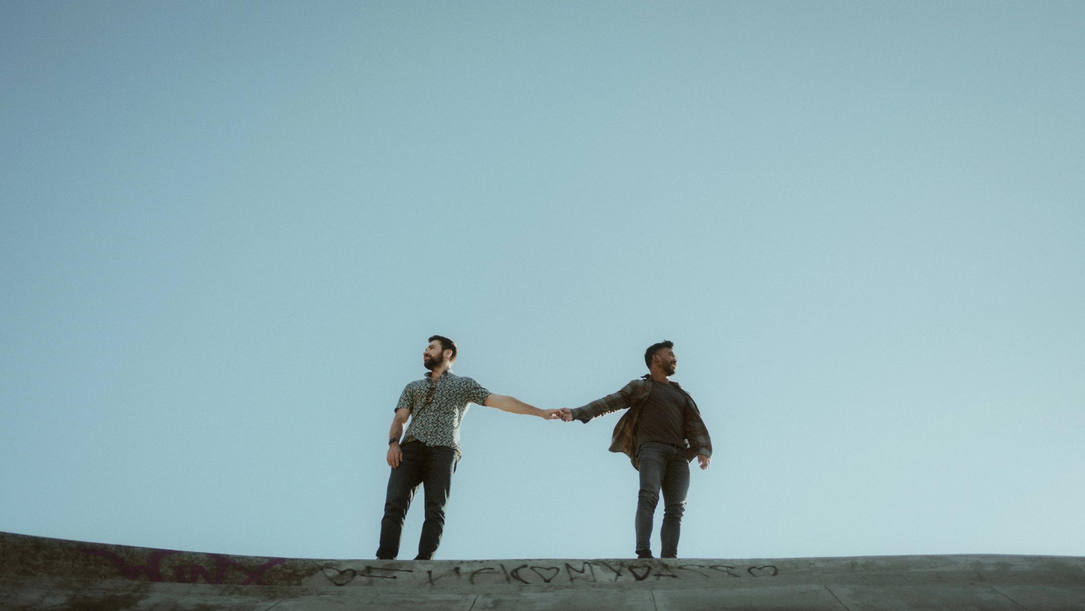 Kris and Ilya hold hands on a curved concrete structure beneath a wide blue sky at Superkilen.