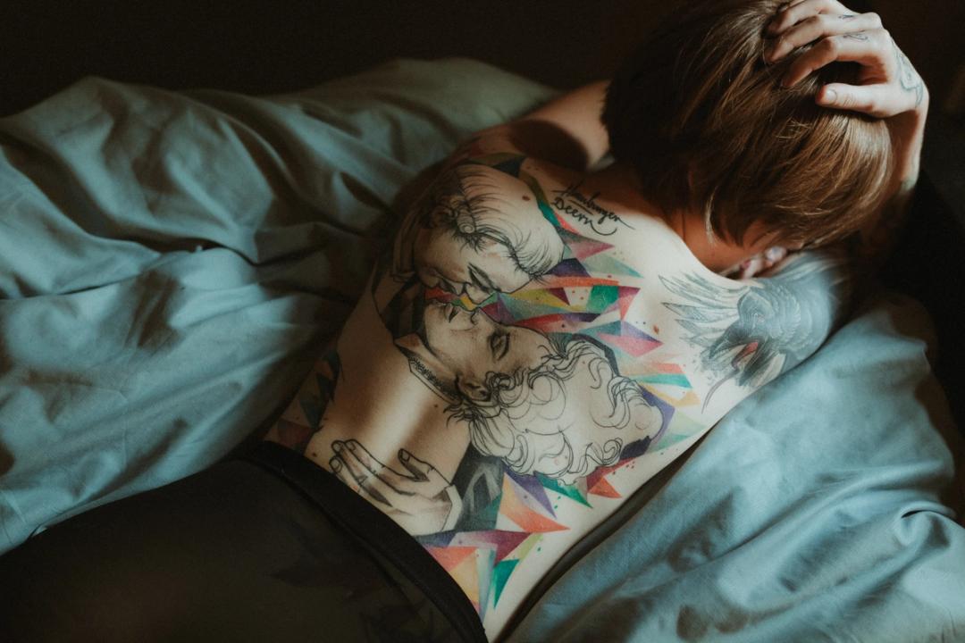 Anki sits on a bed at home in Hamburg, her tattooed back turned toward the camera.