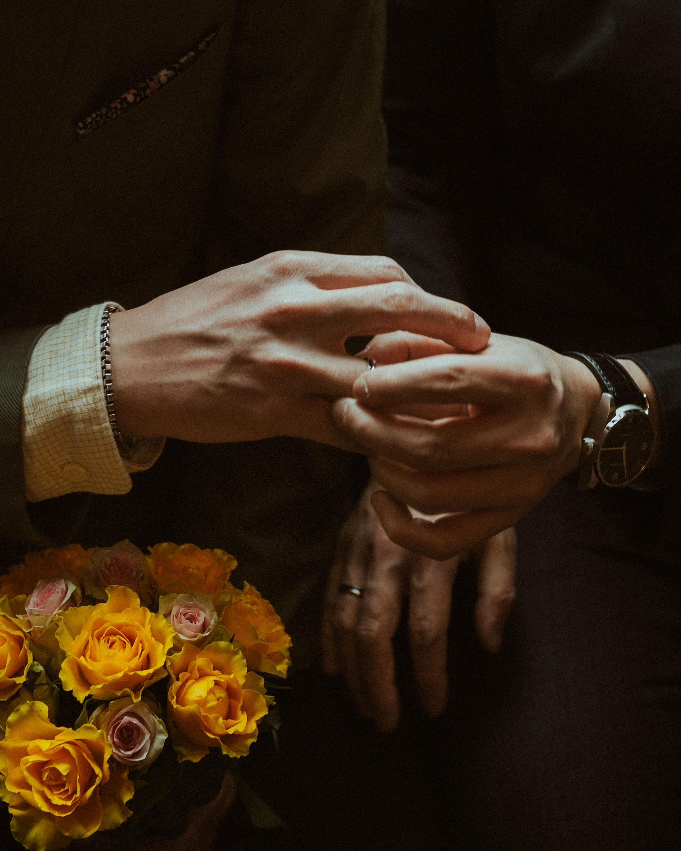 A close view of the newlyweds’ hands, wedding rings and yellow flowers.