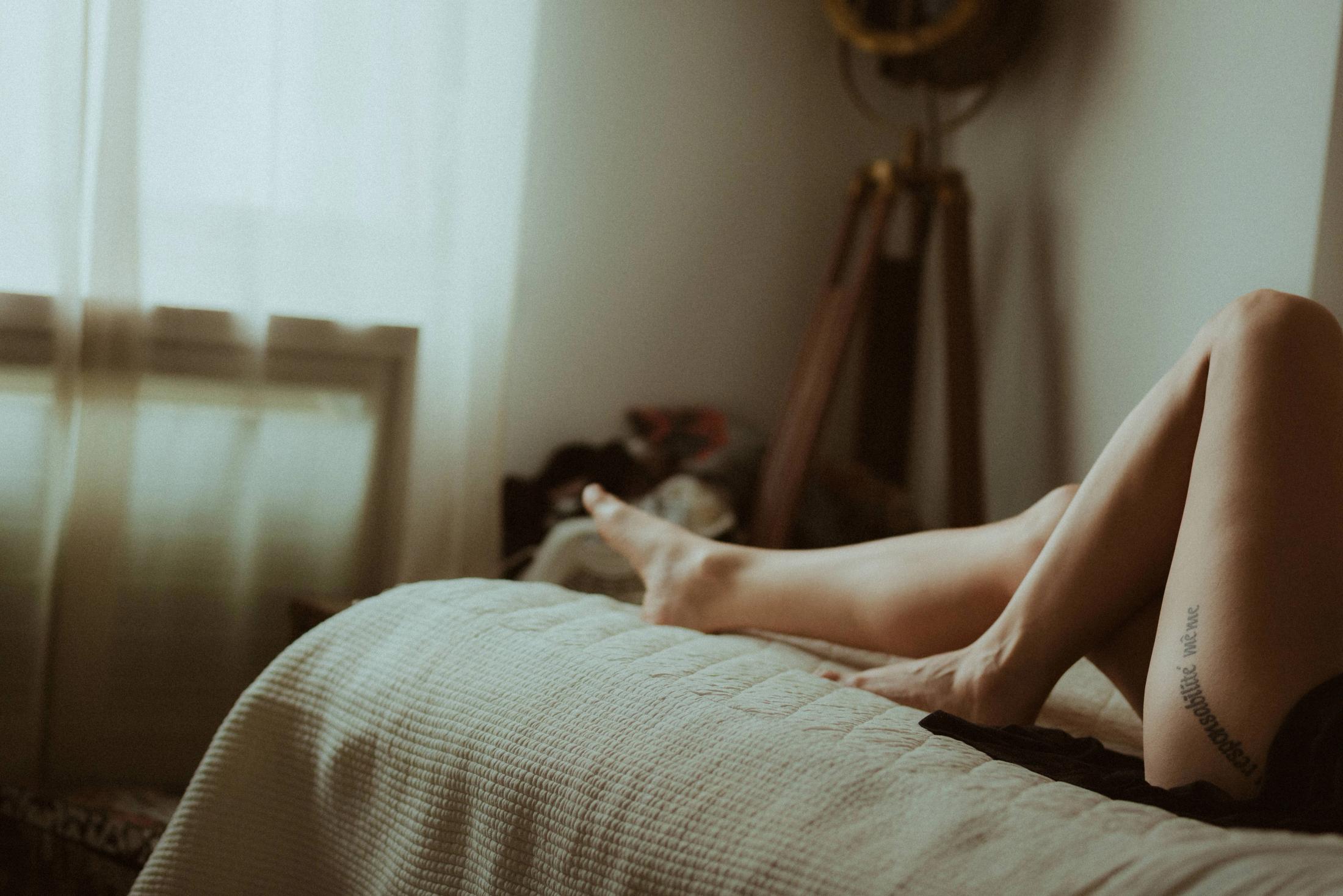 Maya reclining on the bed with her legs raised into the window light.