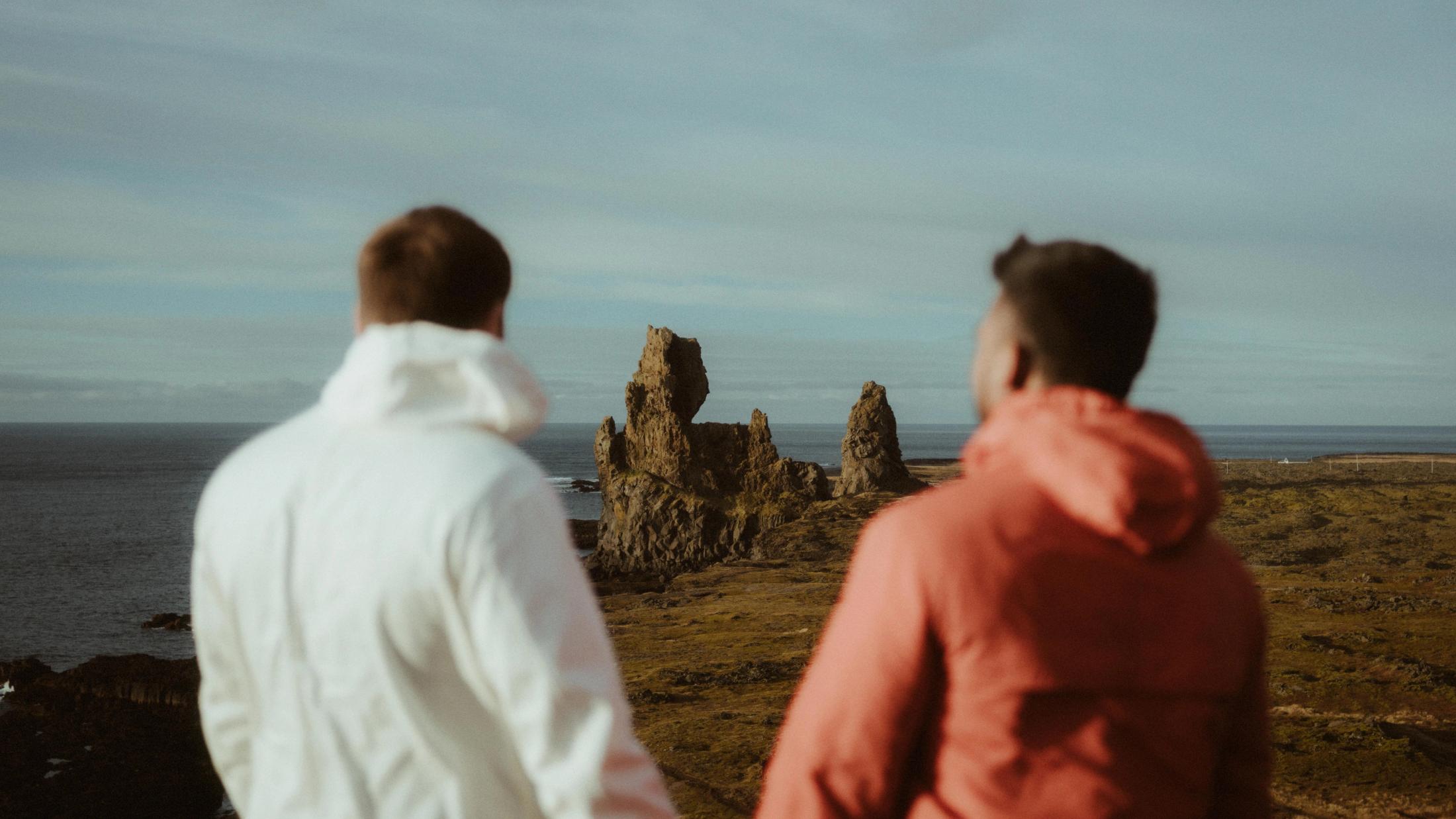 Kris und Ilya stehen in roten und weißen Outdoorjacken gemeinsam an der Küste.