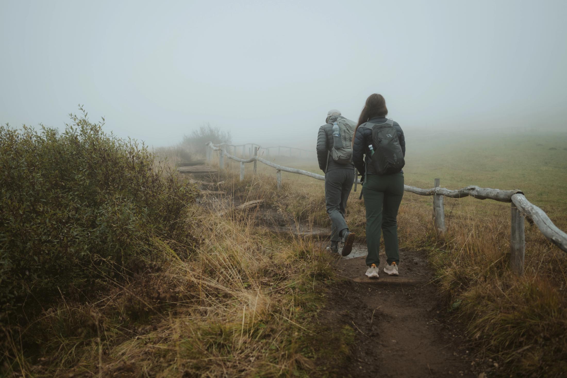 Jana and Steffen walking beside a wooden fence in the fog.