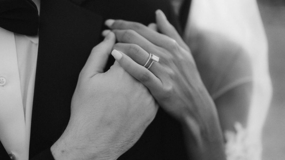 Black-and-white close-up of the bride's ringed hand resting over her partner's hand.