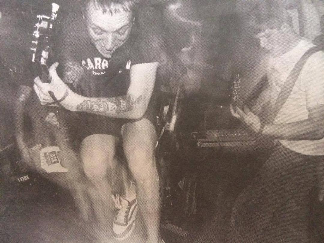 Bjørn jumps with a guitar during a Hoods Up concert while another person plays at right.