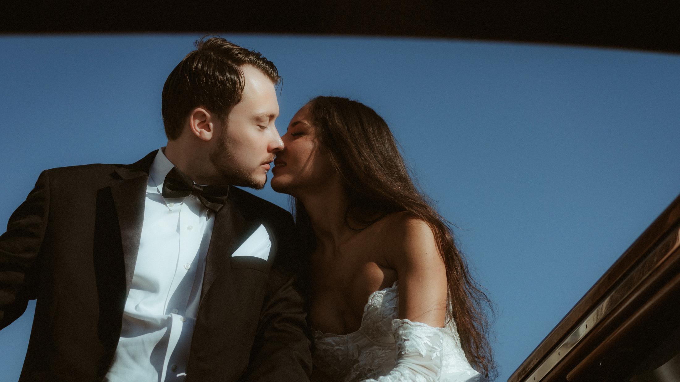 The couple kisses against a deep blue sky inside a polished wooden boat.