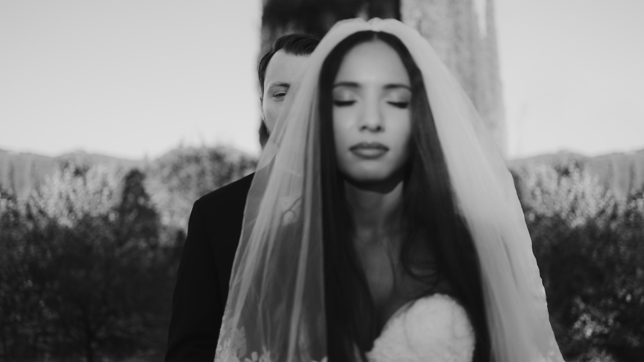 Black-and-white portrait with the bride in the foreground and her partner partly hidden behind her veil.