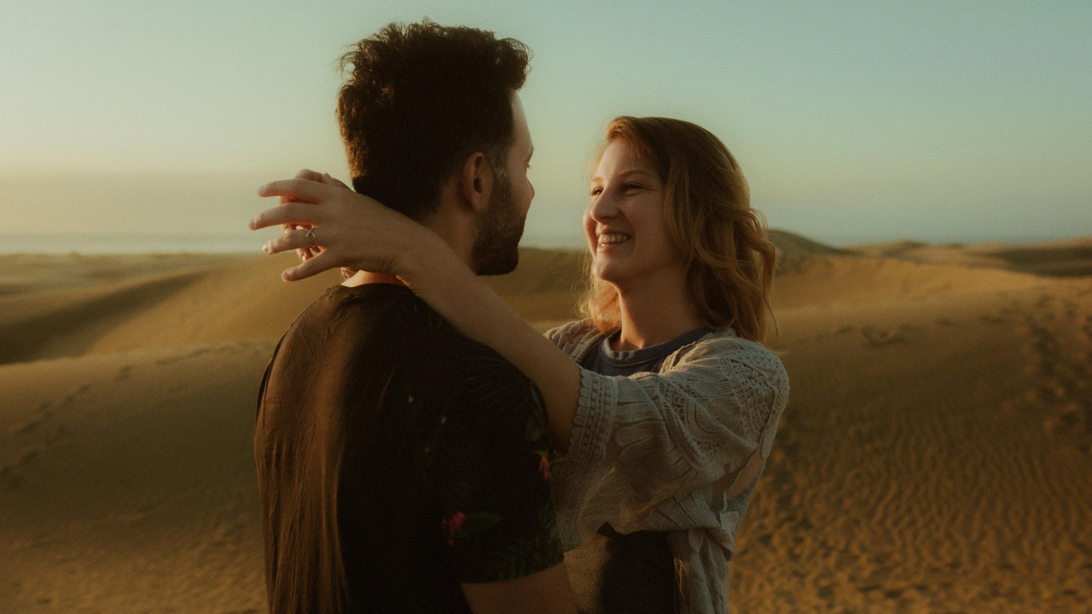 Katja laughing as she puts her arms around David in the dunes.