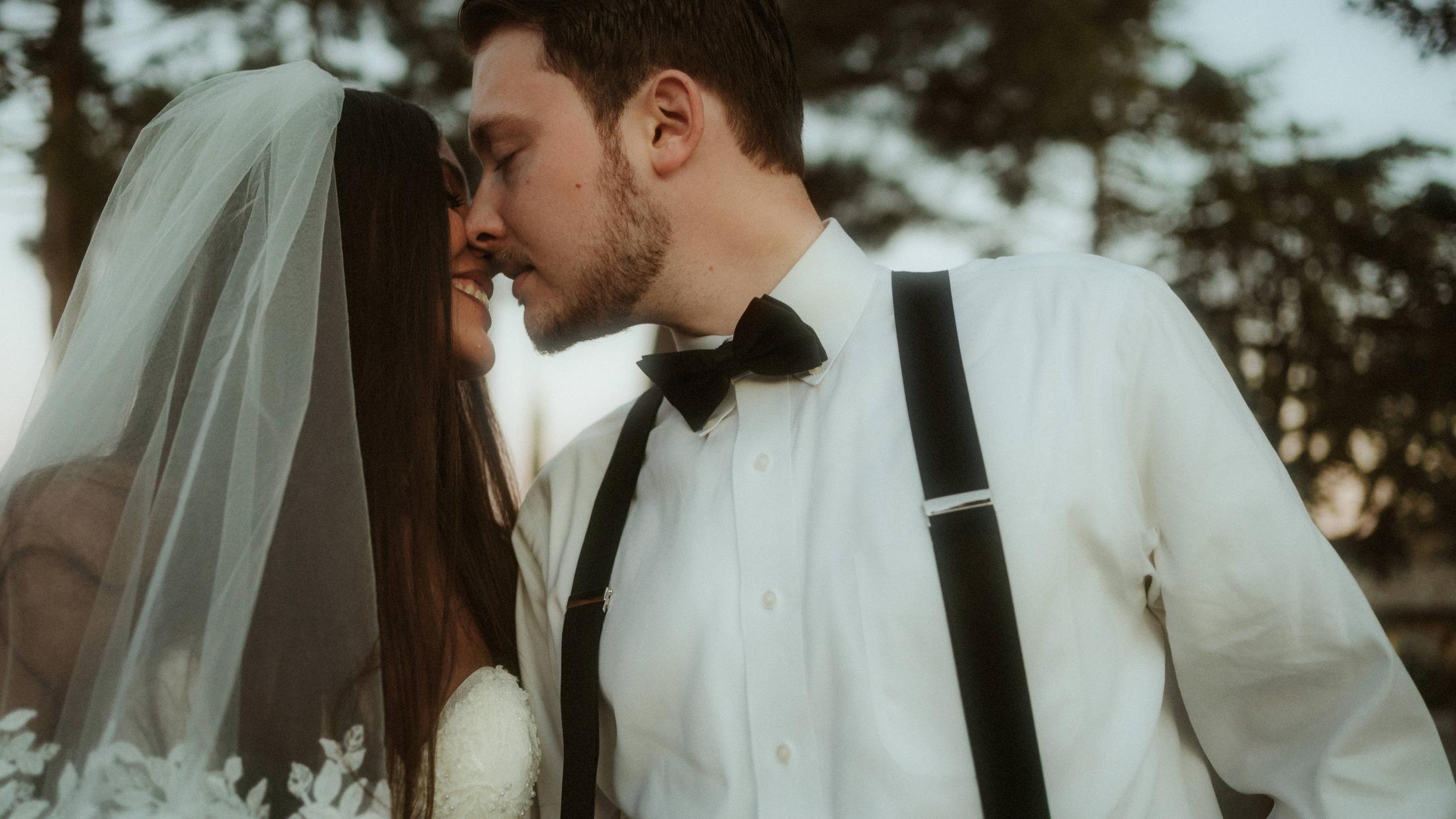 The couple rests their foreheads together beneath trees in the evening light.