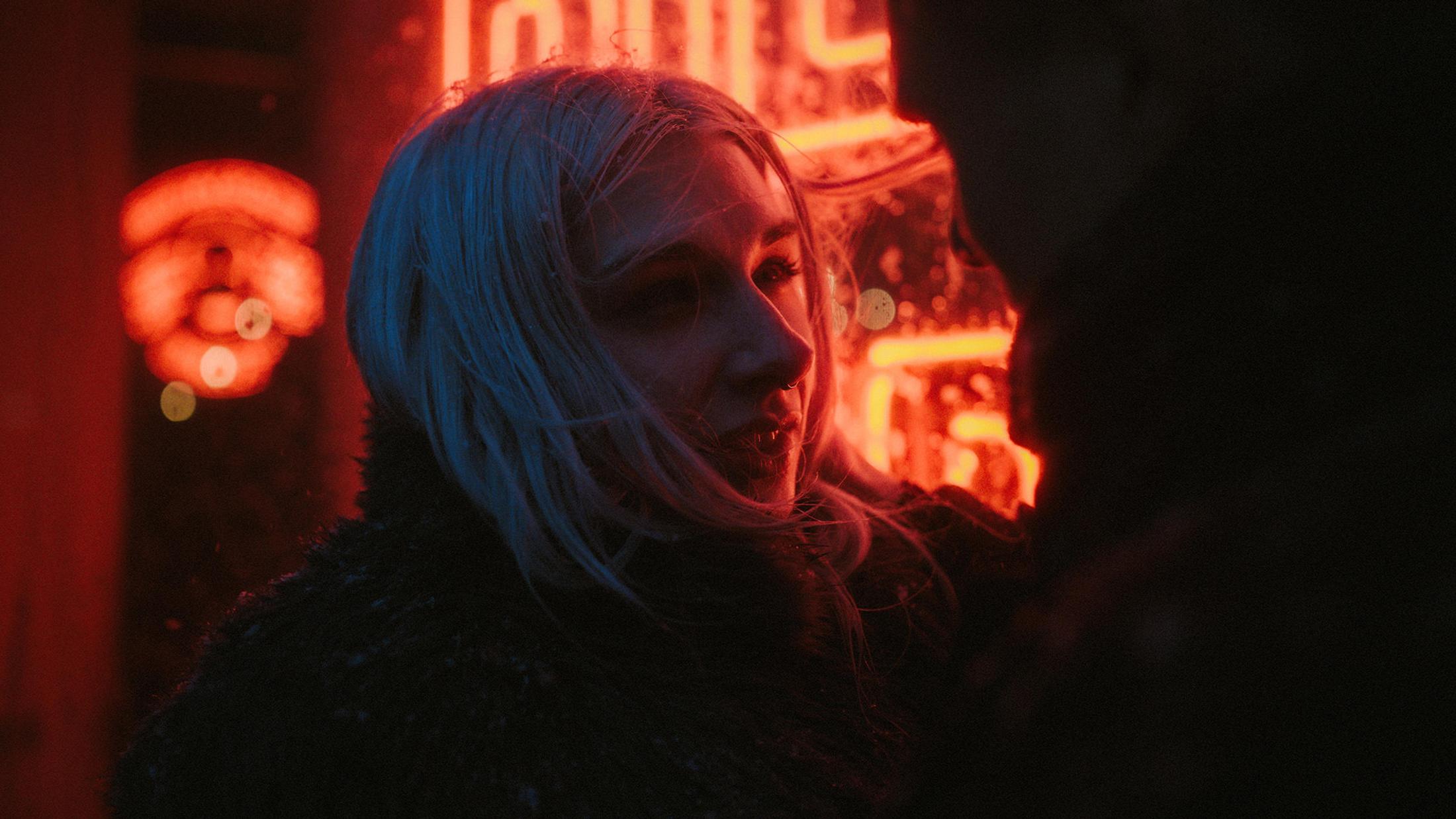 Neon light colours Lorelai's face blue and red as snow falls around her.