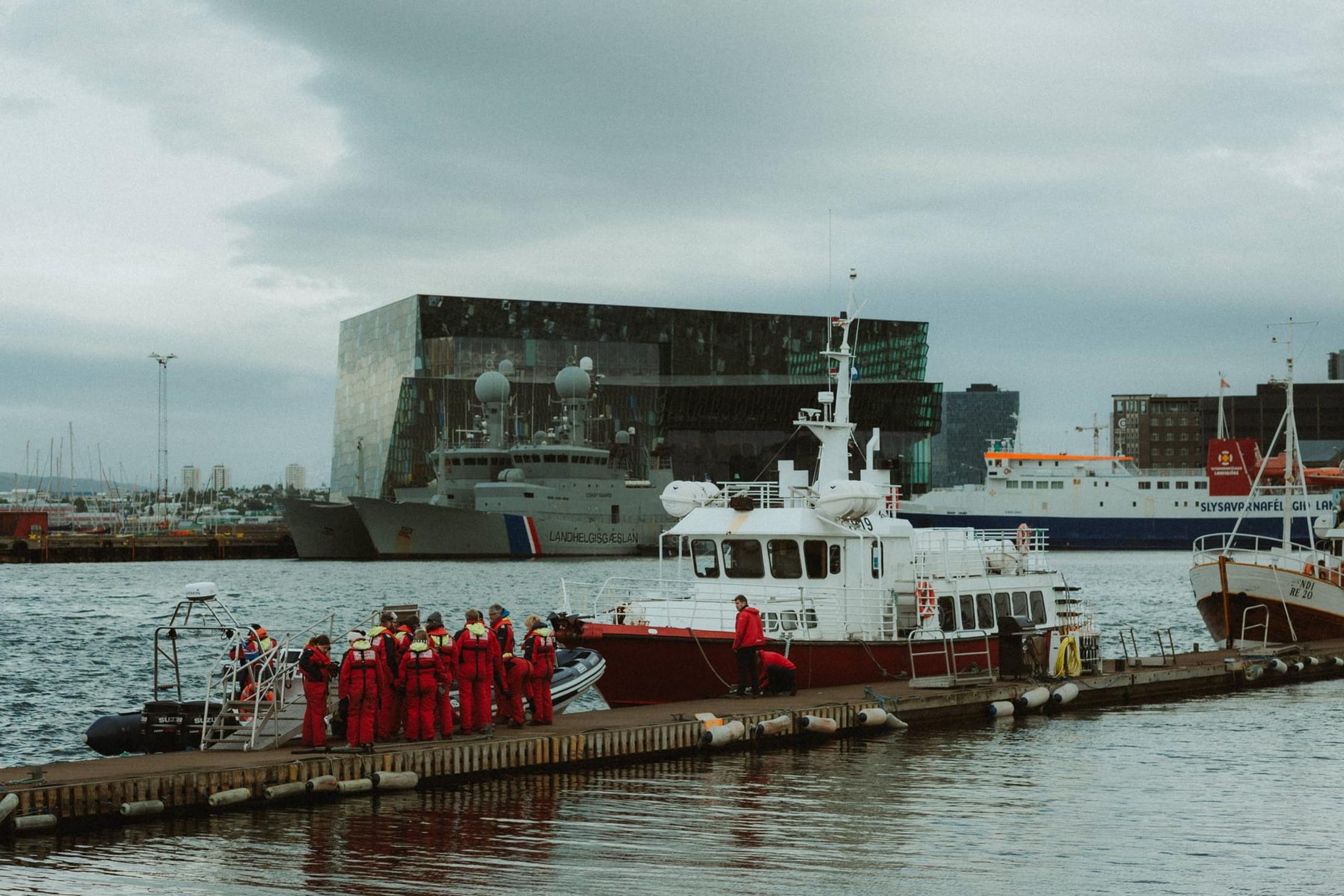 Boats beside a quay, with the glass facade of Harpa behind them.