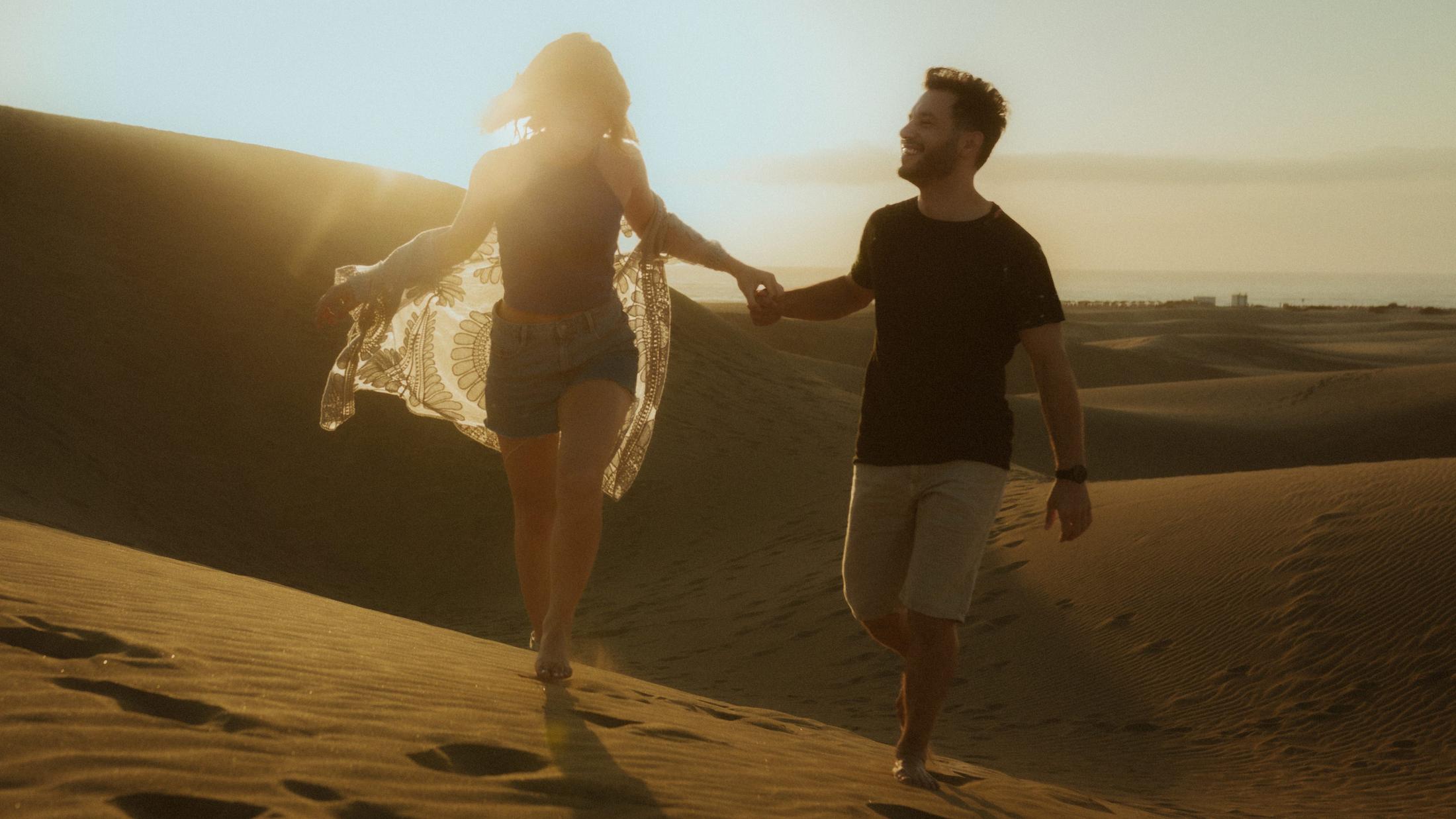 Katja and David running hand in hand with the dunes behind them.