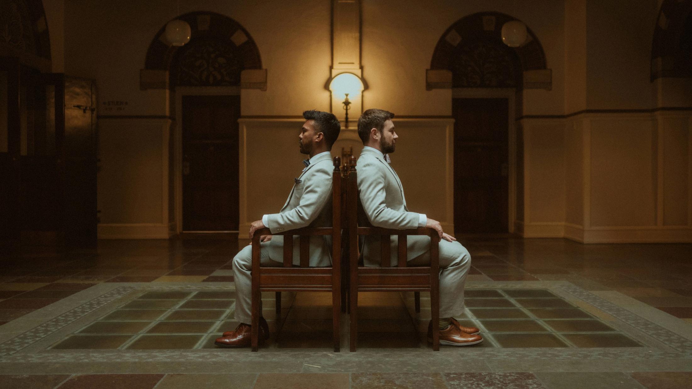 Wide symmetrical view of Kris and Ilya sitting back to back on a bench inside City Hall.