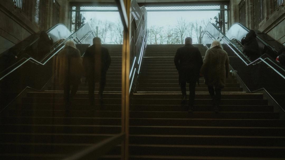 Lorelai and Steffen climb a station staircase beside their mirrored reflection.