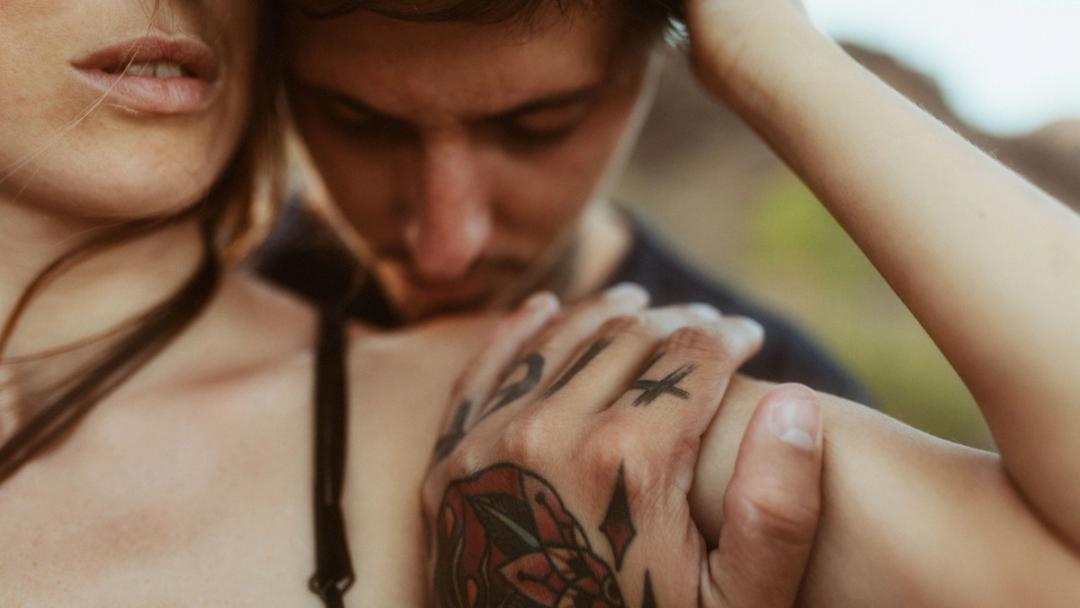 Detailaufnahme von Händen und einem Tattoo während eines Kusses.