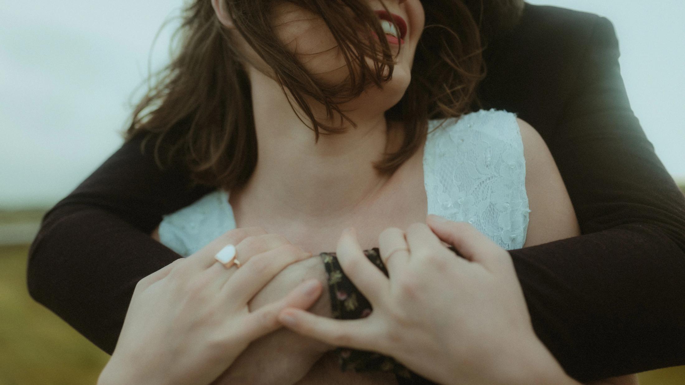 Anni's hands rest over Daniel's arms against the white lace dress.