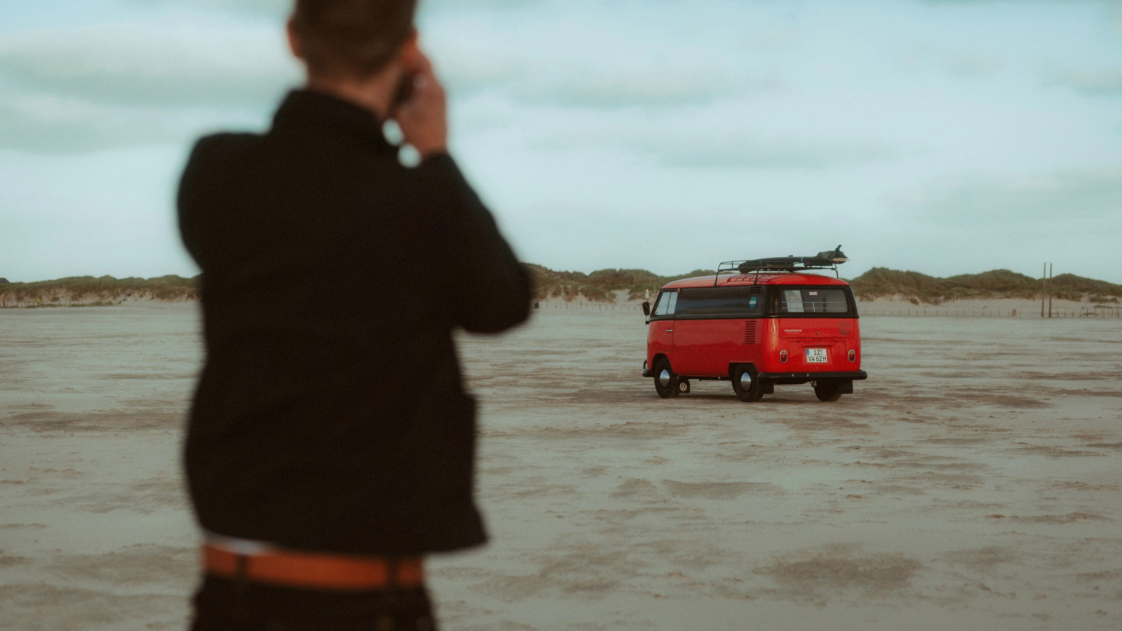 A person looks across the beach toward a red camper van in St. Peter-Ording.
