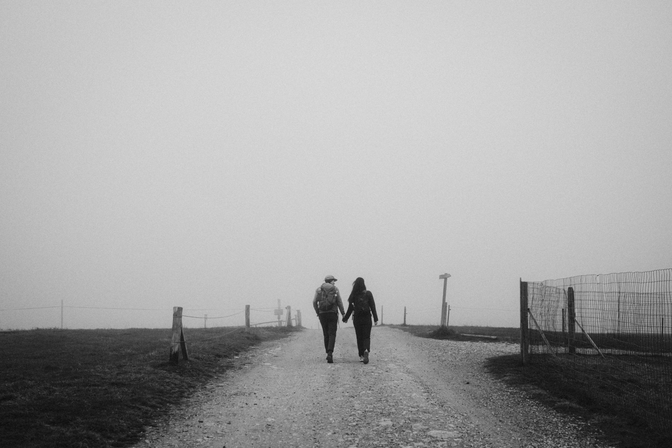 Jana and Steffen walking together into fog along a pale mountain path.